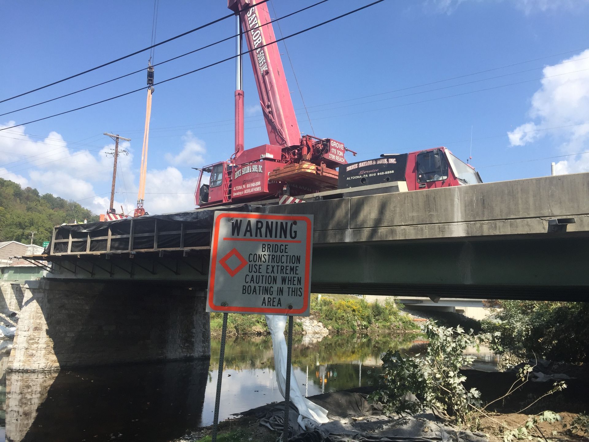 Bridge under repair with red crane above warning sign over water