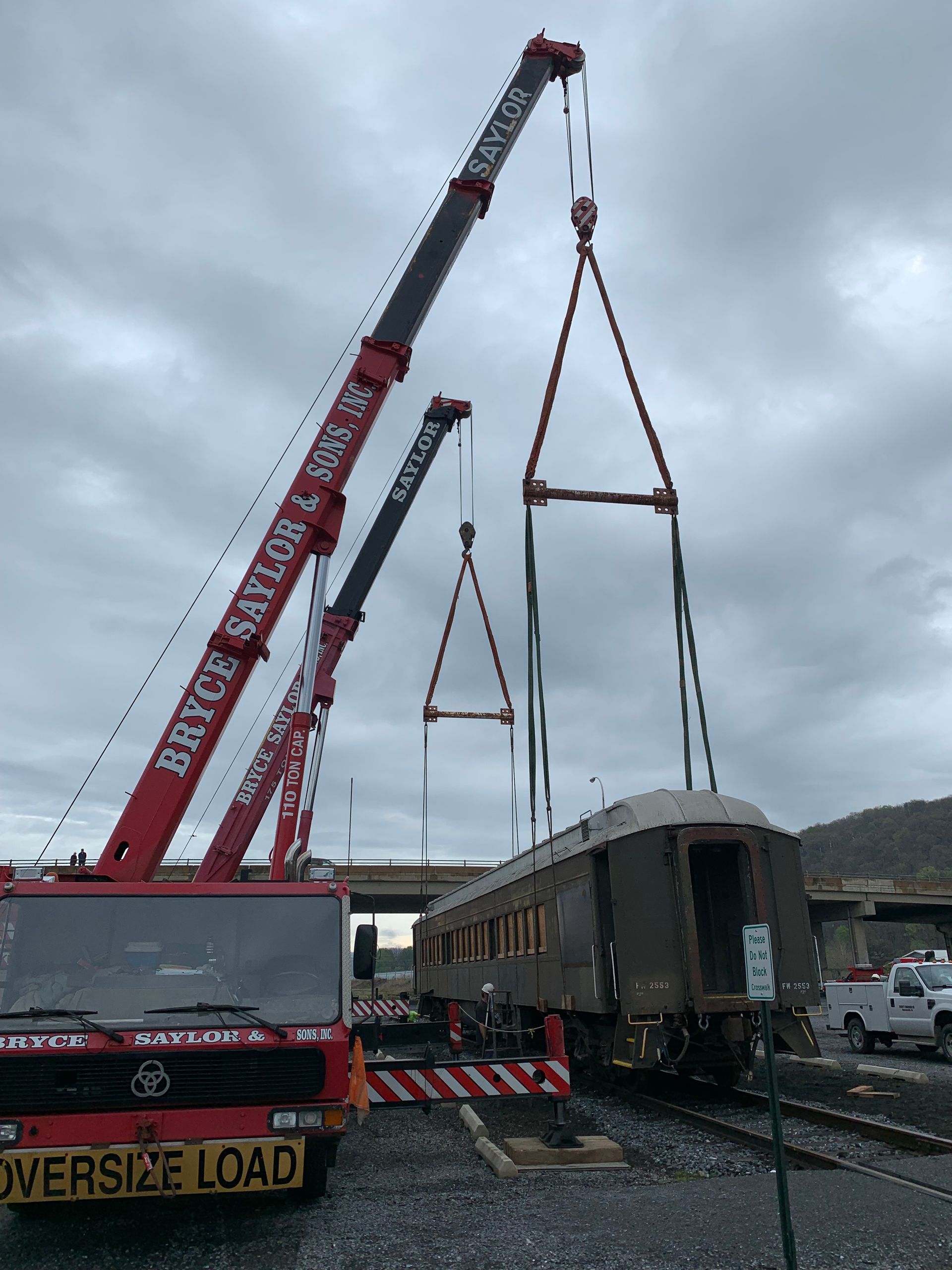 Red crane lifting a railcar beside a track under cloudy skies