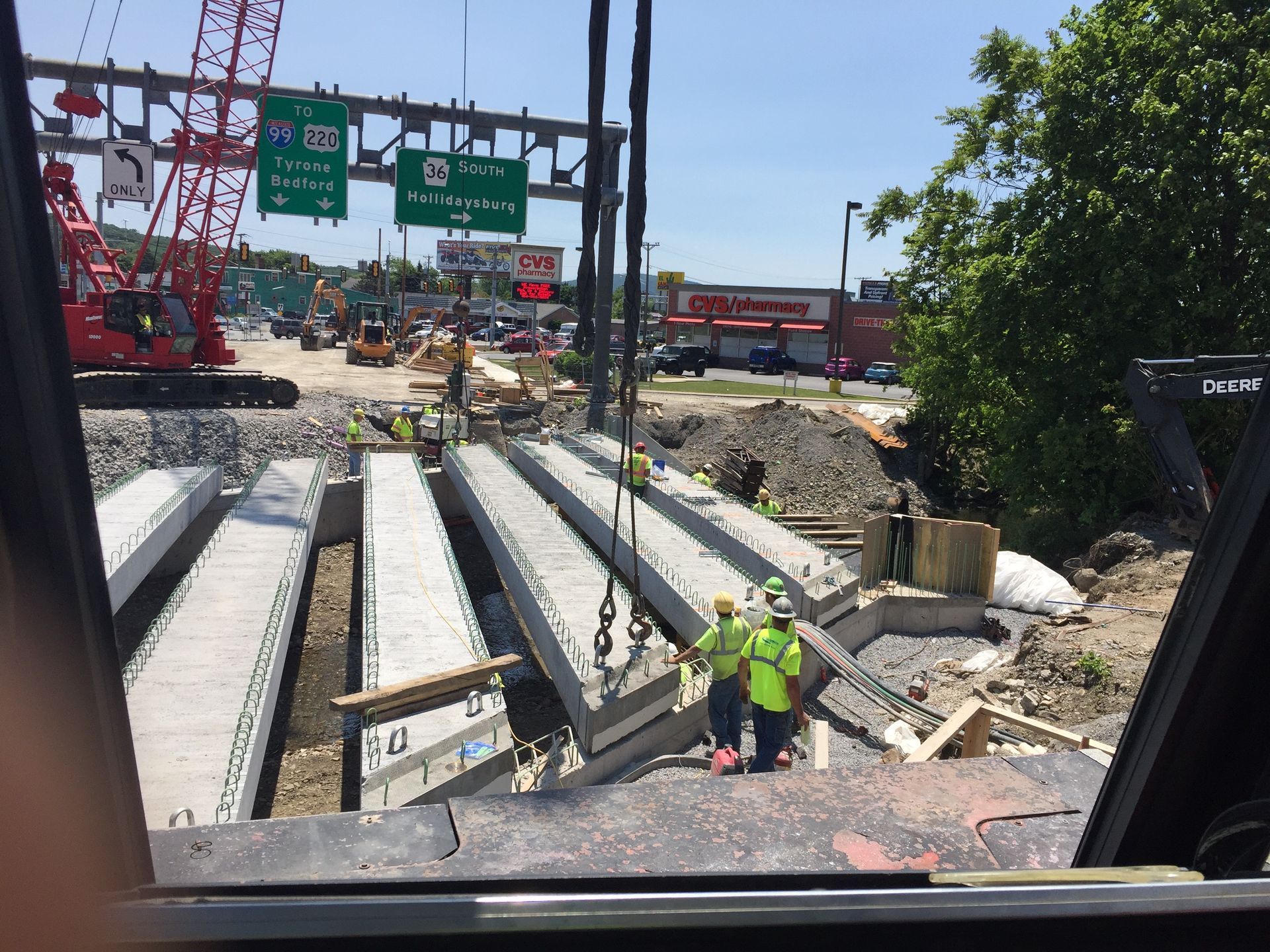 Railroad construction site with workers in neon vests and stacked concrete beams under highway signs