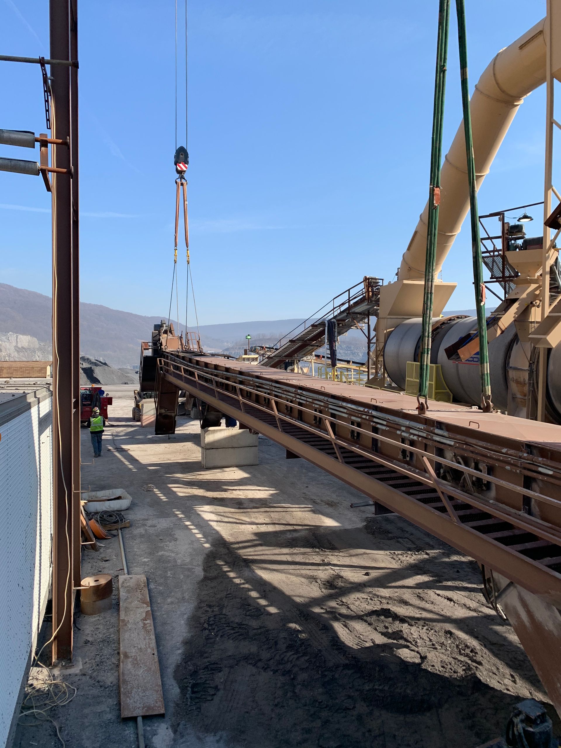 Construction workers lifting a long steel beam with a crane on a bridge site under a clear blue sky