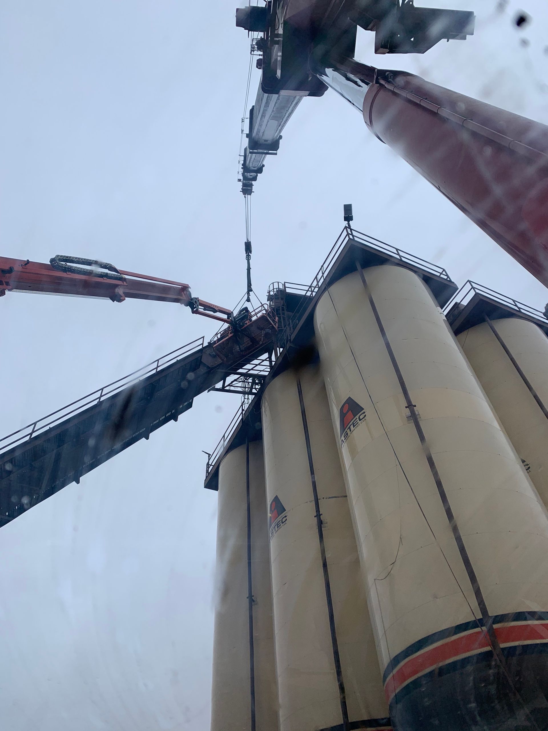 Upward view of grain silos and conveyor arms against a cloudy sky