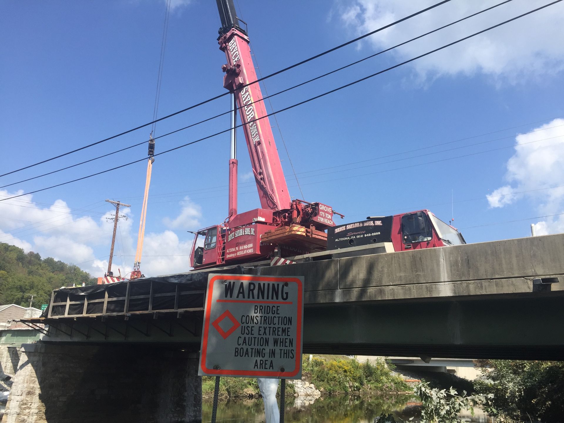 Pink crane lifting equipment on a bridge beside a warning sign under a blue sky