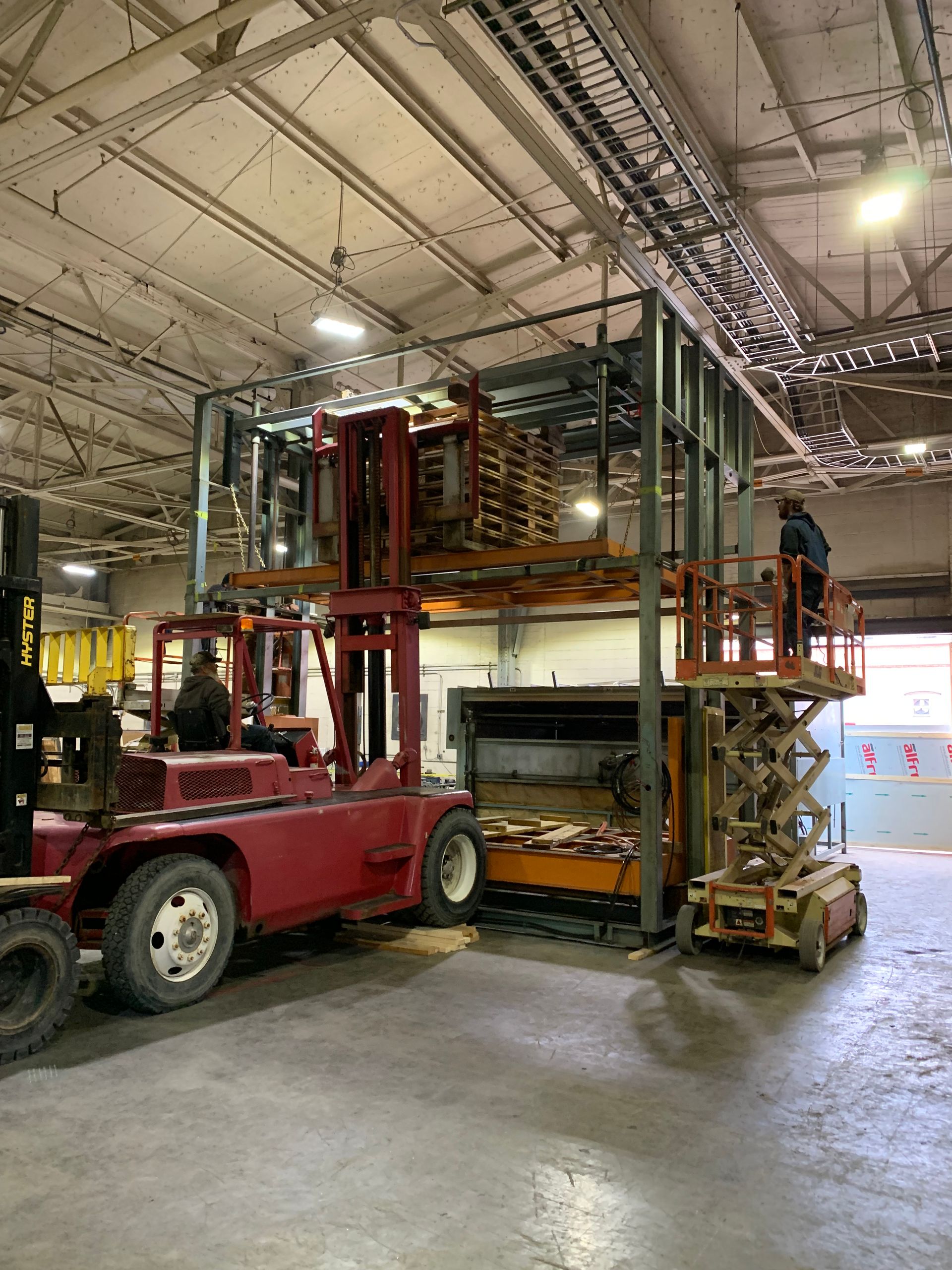 Red forklift lifting a tall metal storage rack in a warehouse