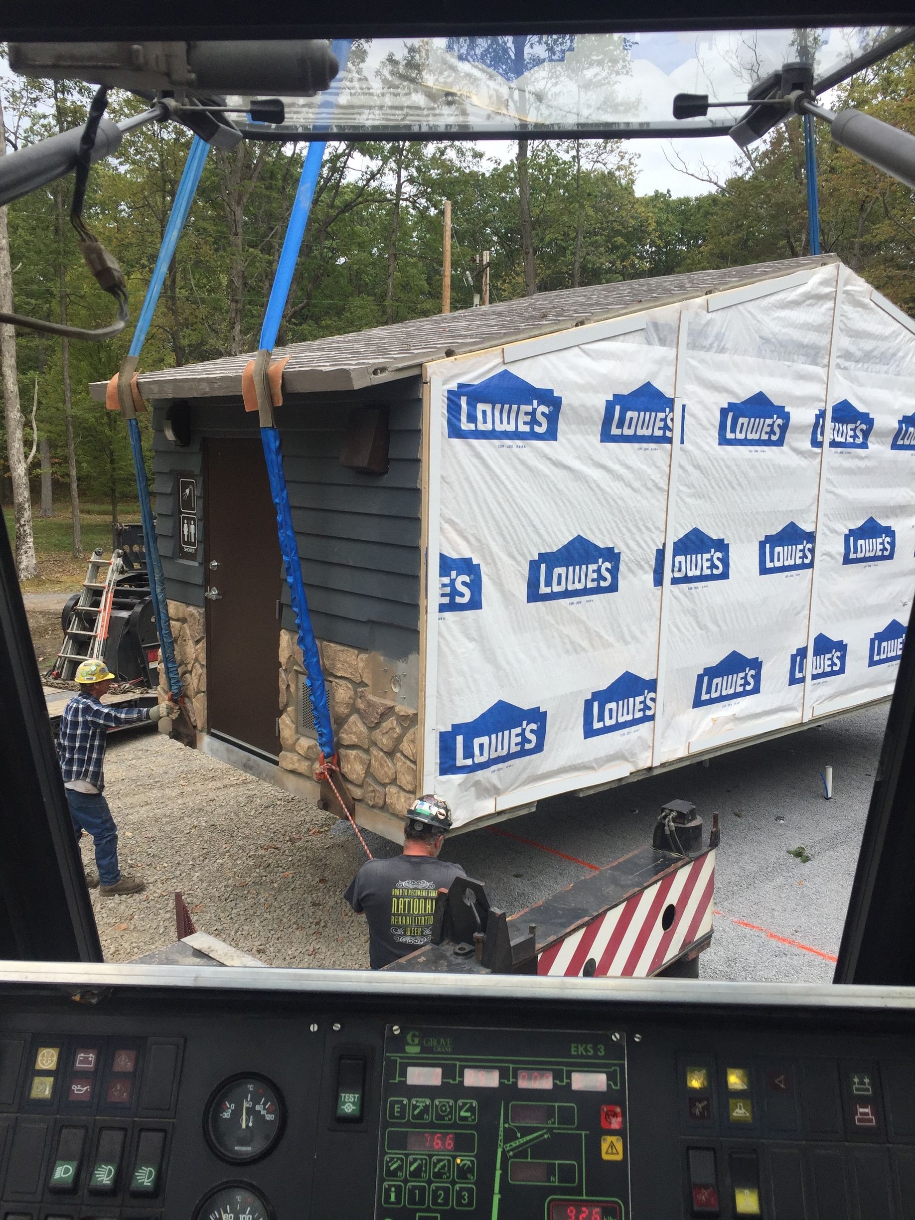 Crane lifting a small shed wrapped in Lowe’s house wrap at a construction site