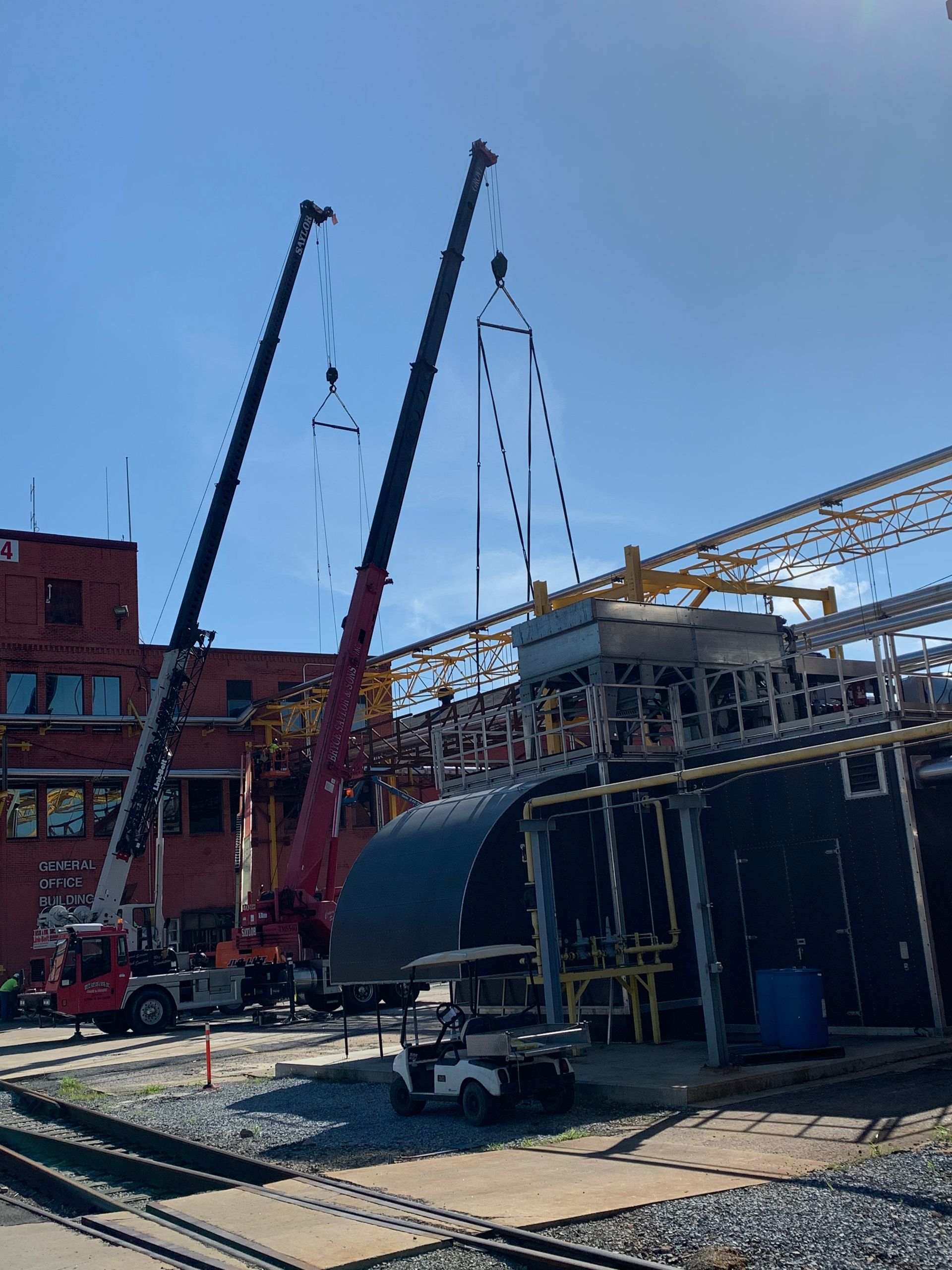 Construction site with two red cranes lifting steel framing beside a brick building