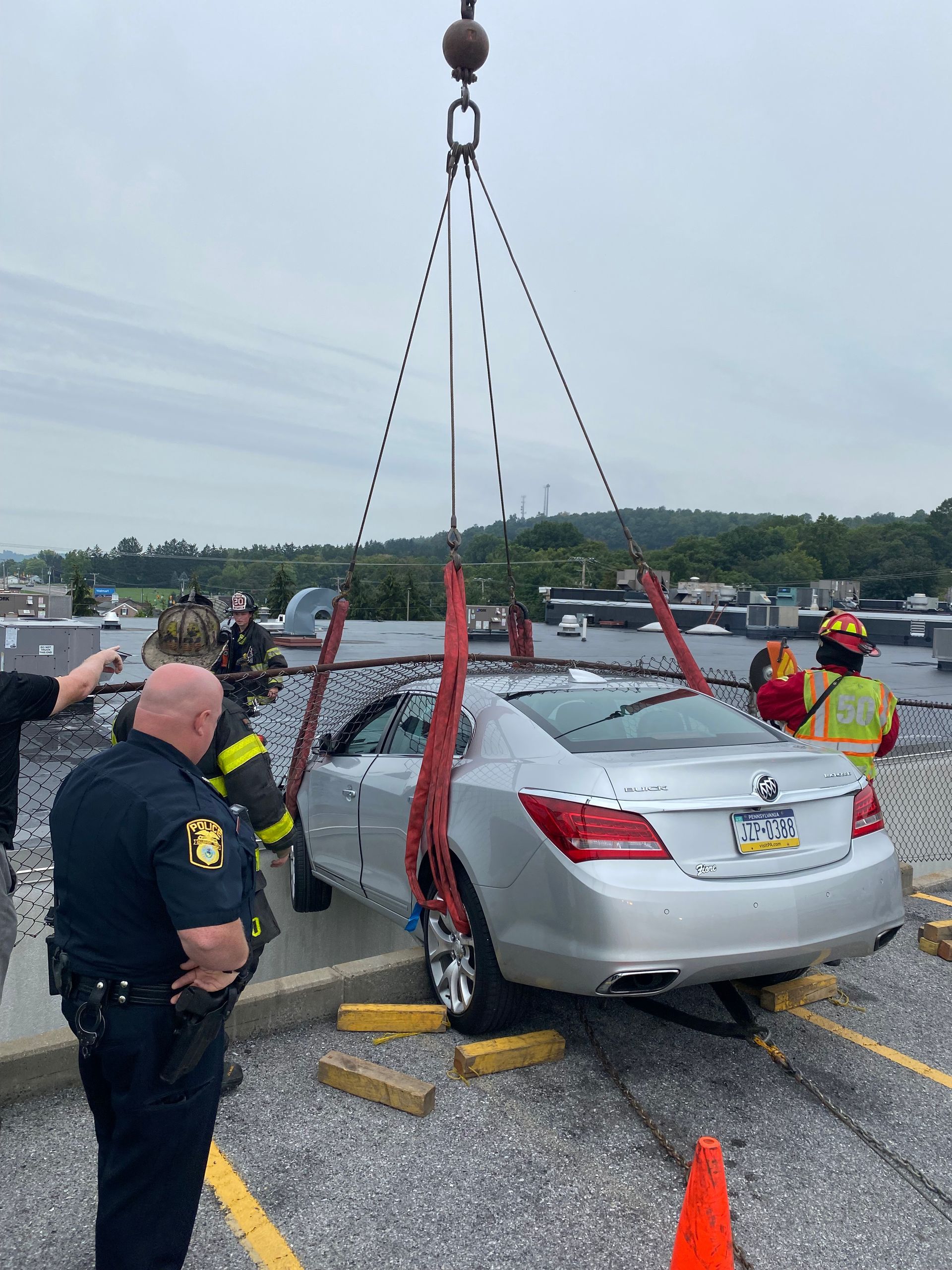Silver sedan being lifted by crane after crash, with responders in safety vests on a highway shoulder