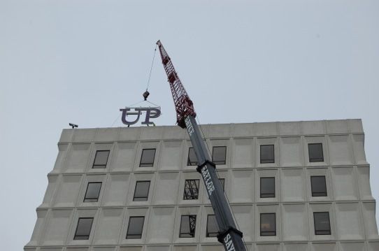 Crane beside a white building with the letters “UP” on the roof against a gray sky