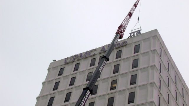 A tall building with a crane reaching up its side against a cloudy sky.