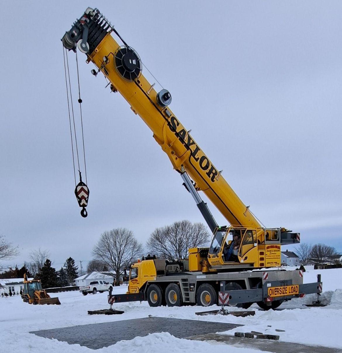 Yellow mobile crane in a snowy field with its boom raised and hook hanging overhead.