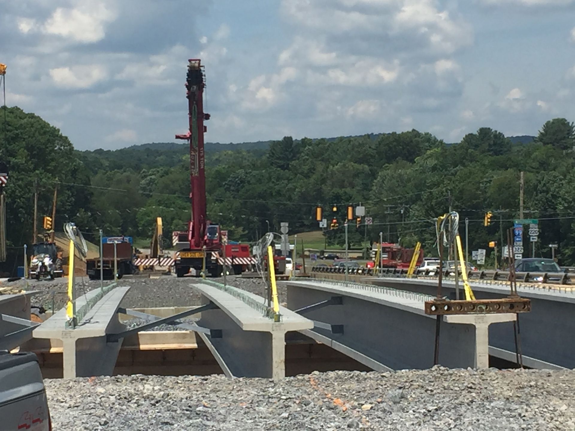 Construction site with steel bridge beams, crane, and workers under a cloudy sky
