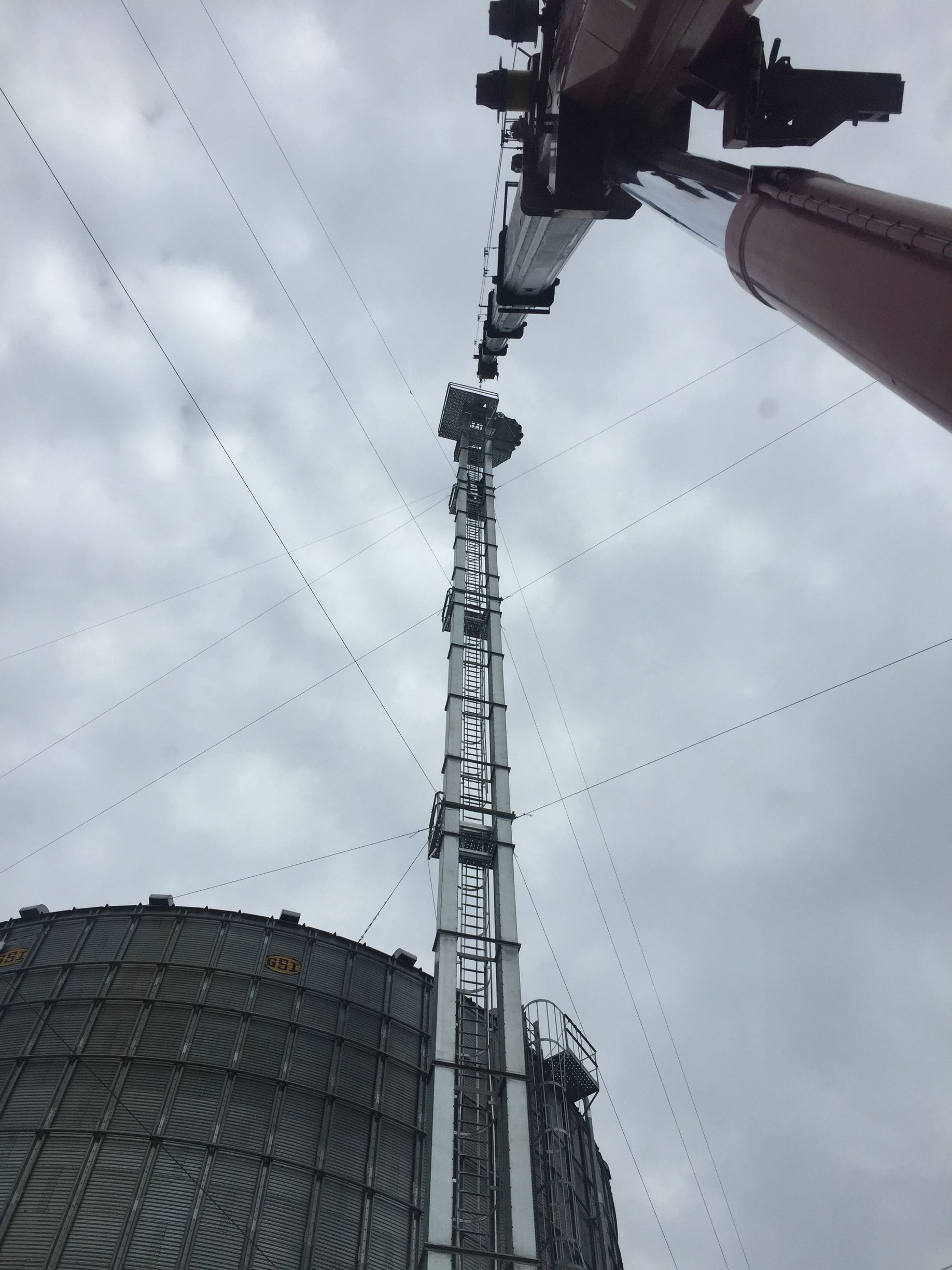 Tall crane beside a large cylindrical structure under a cloudy sky, viewed from below