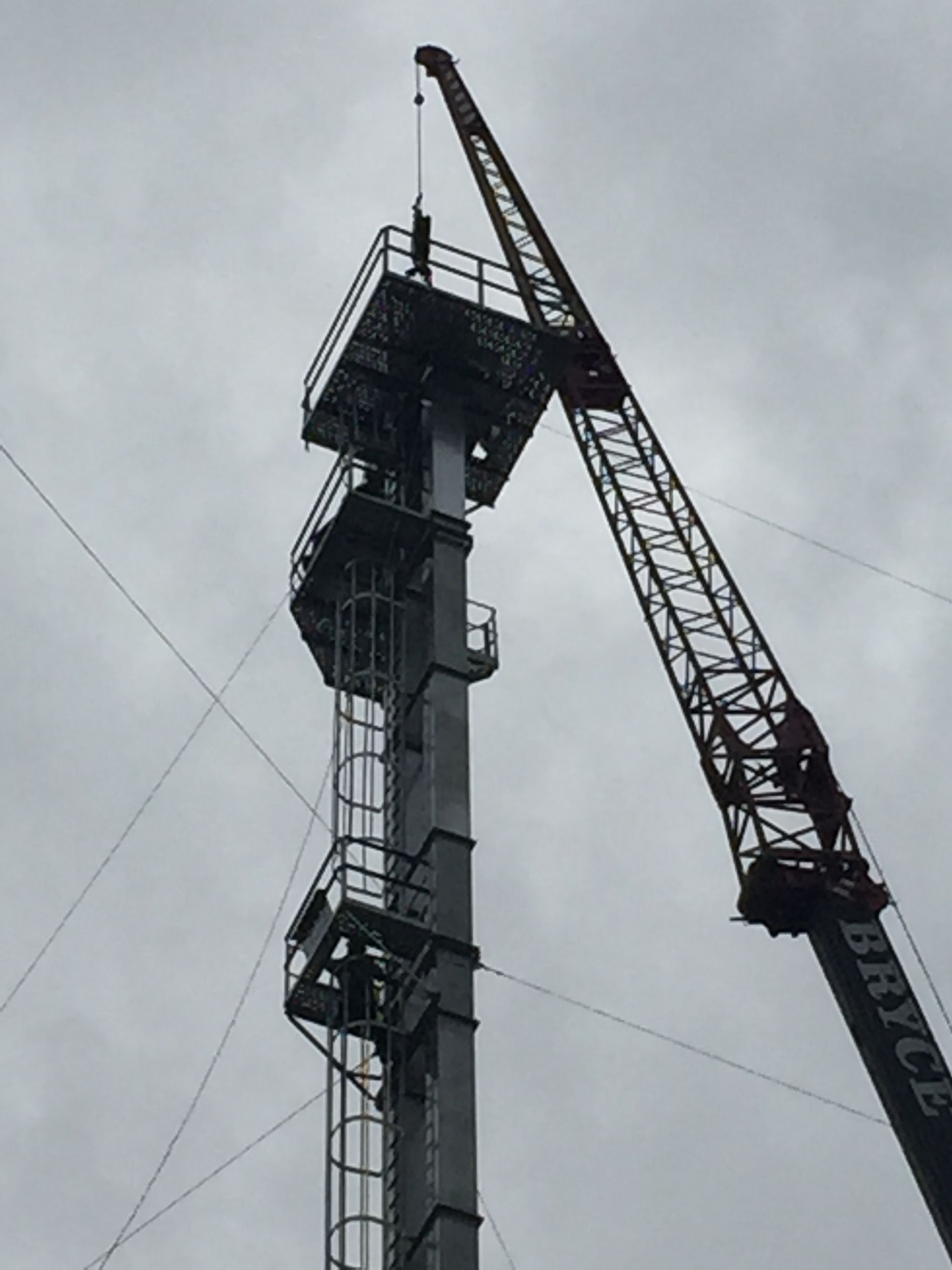 Tall construction crane beside a high steel tower against a gray sky