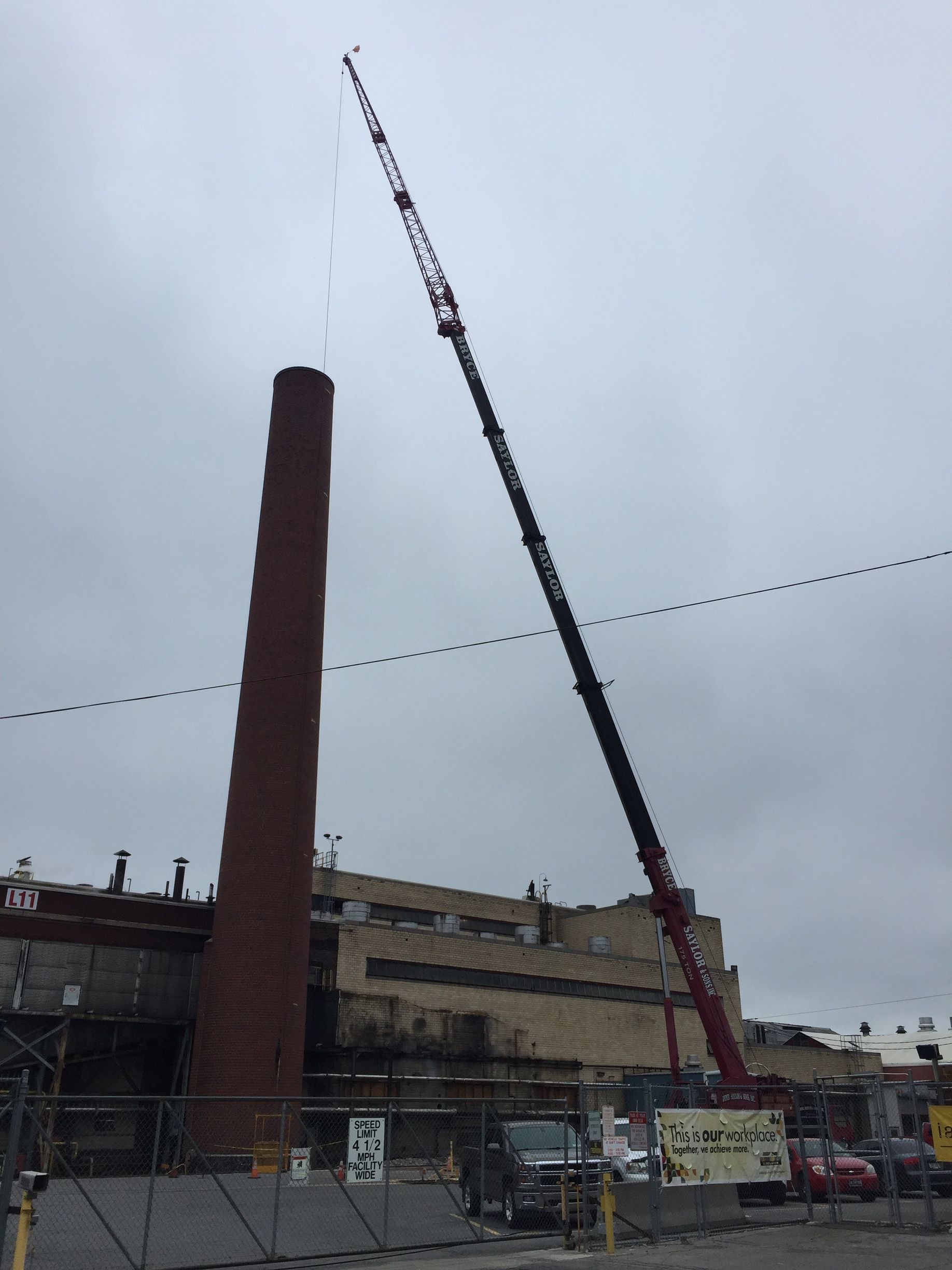 Tall brick smokestack beside a red crane at an industrial site under a cloudy sky