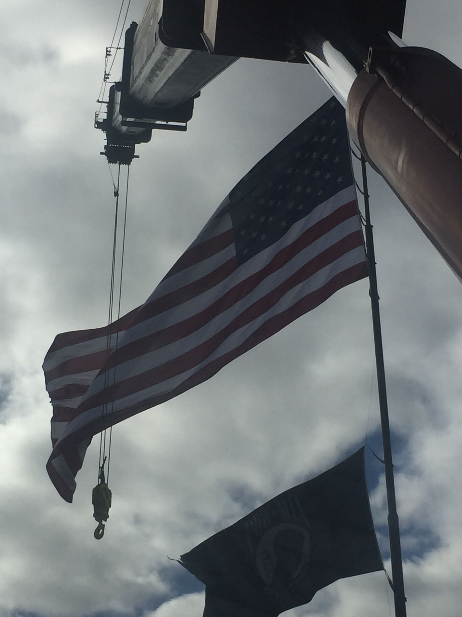 American flag hanging from a crane against a cloudy sky, with a second flag below.