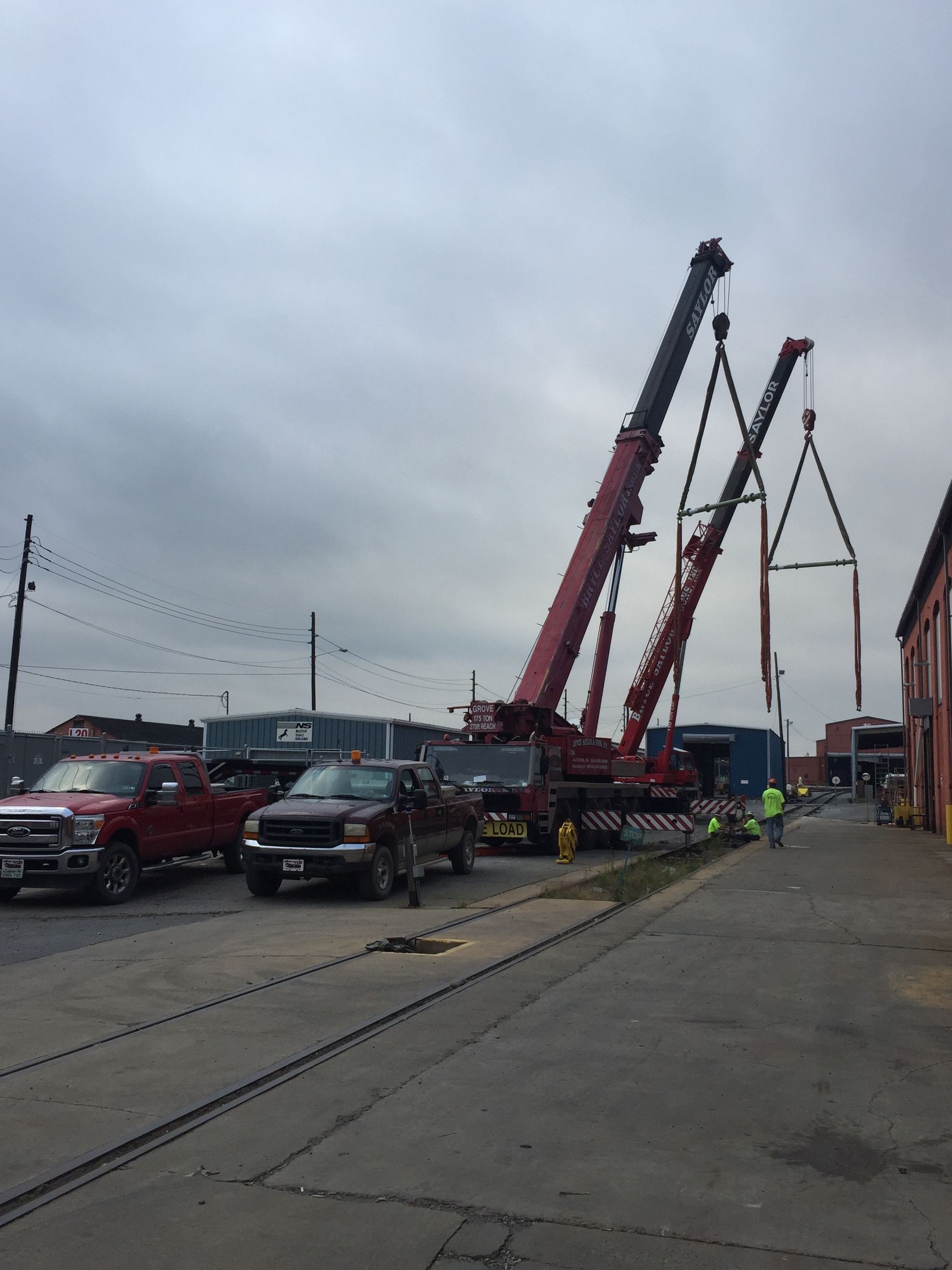 Several tow trucks and cranes line a dockside road under a gray sky.
