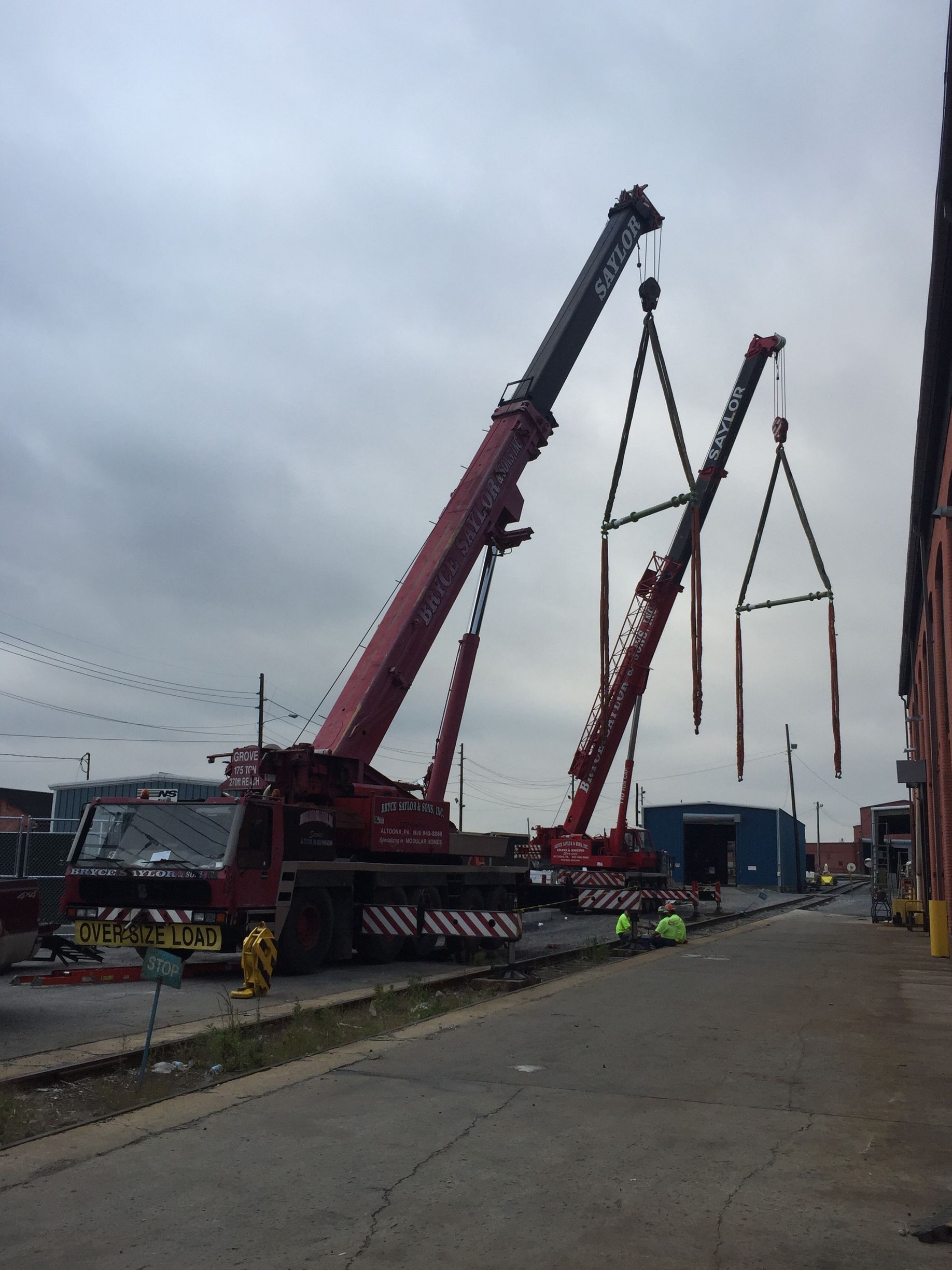 Cranes lifting long poles at a construction site under a gray sky.