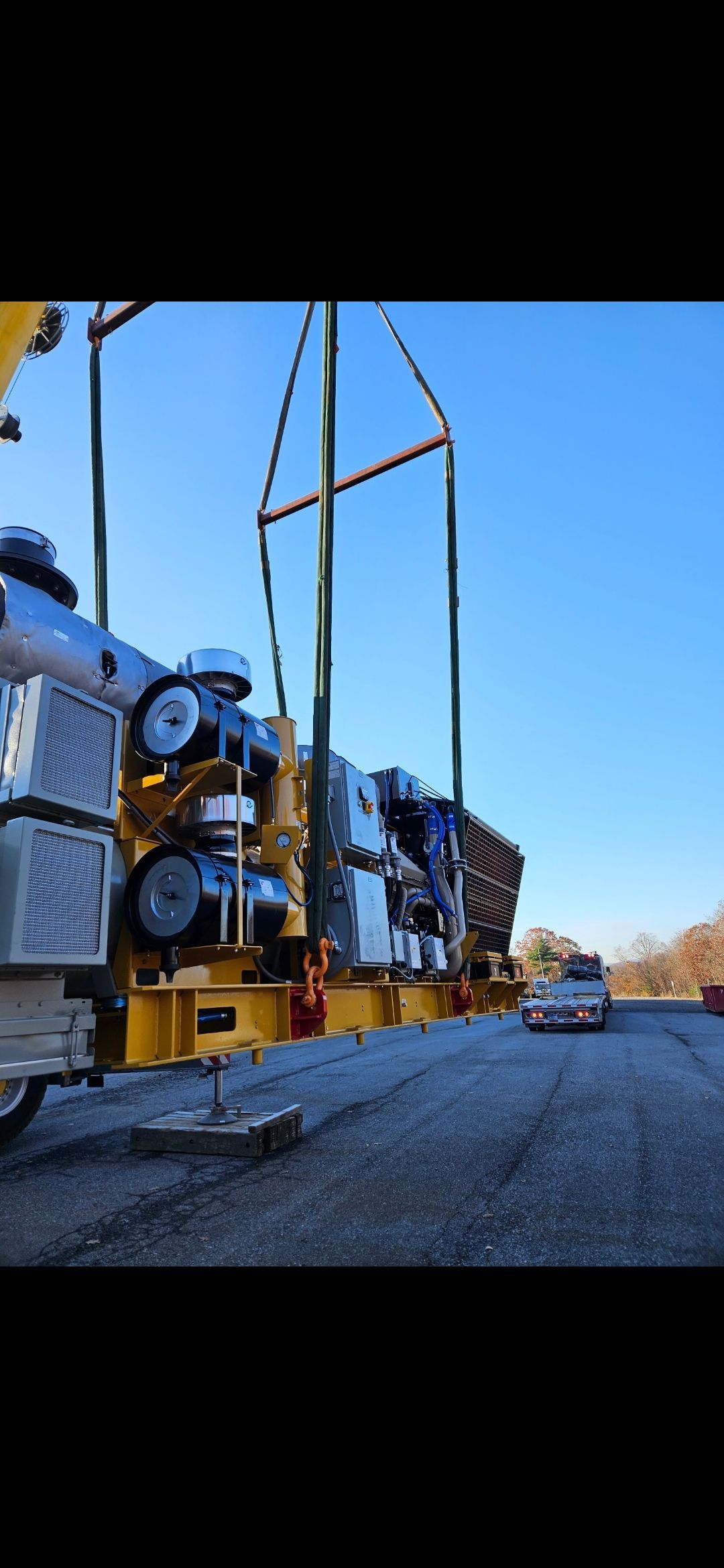 Flatbed truck hauling large industrial equipment on a gravel road under a blue sky