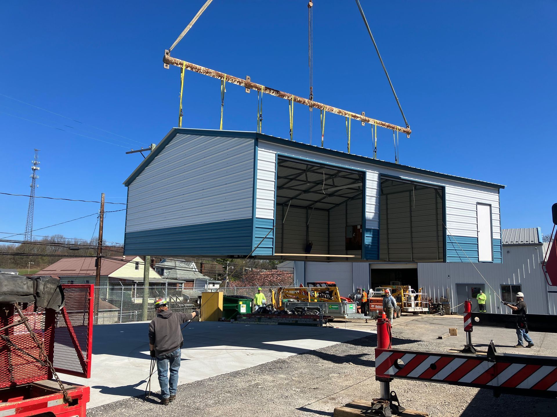 Large modular building suspended by crane over a construction site with workers below