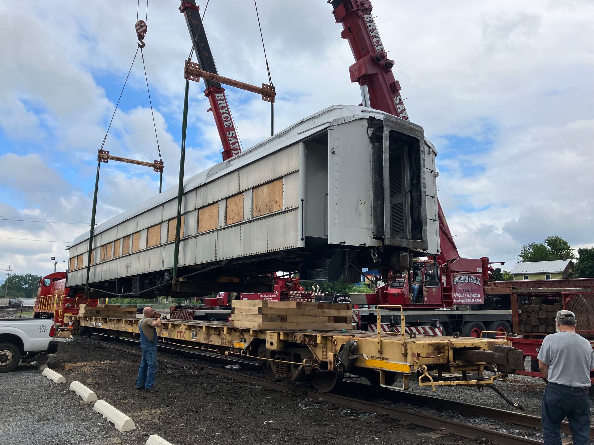 Large industrial machine being lifted by cranes onto a flatbed trailer in a muddy work site