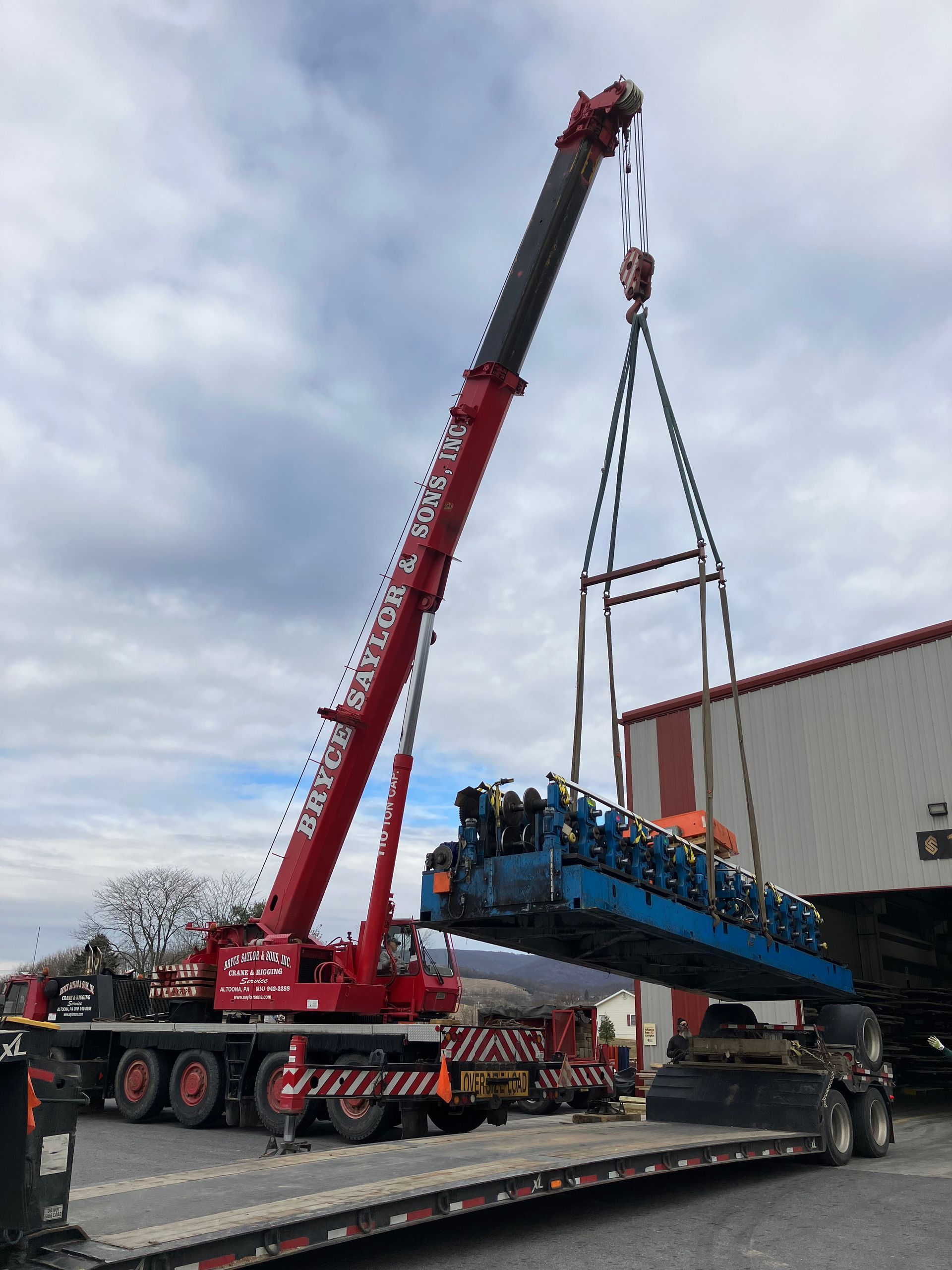 Red crane lifting a blue industrial machine onto a flatbed truck outdoors