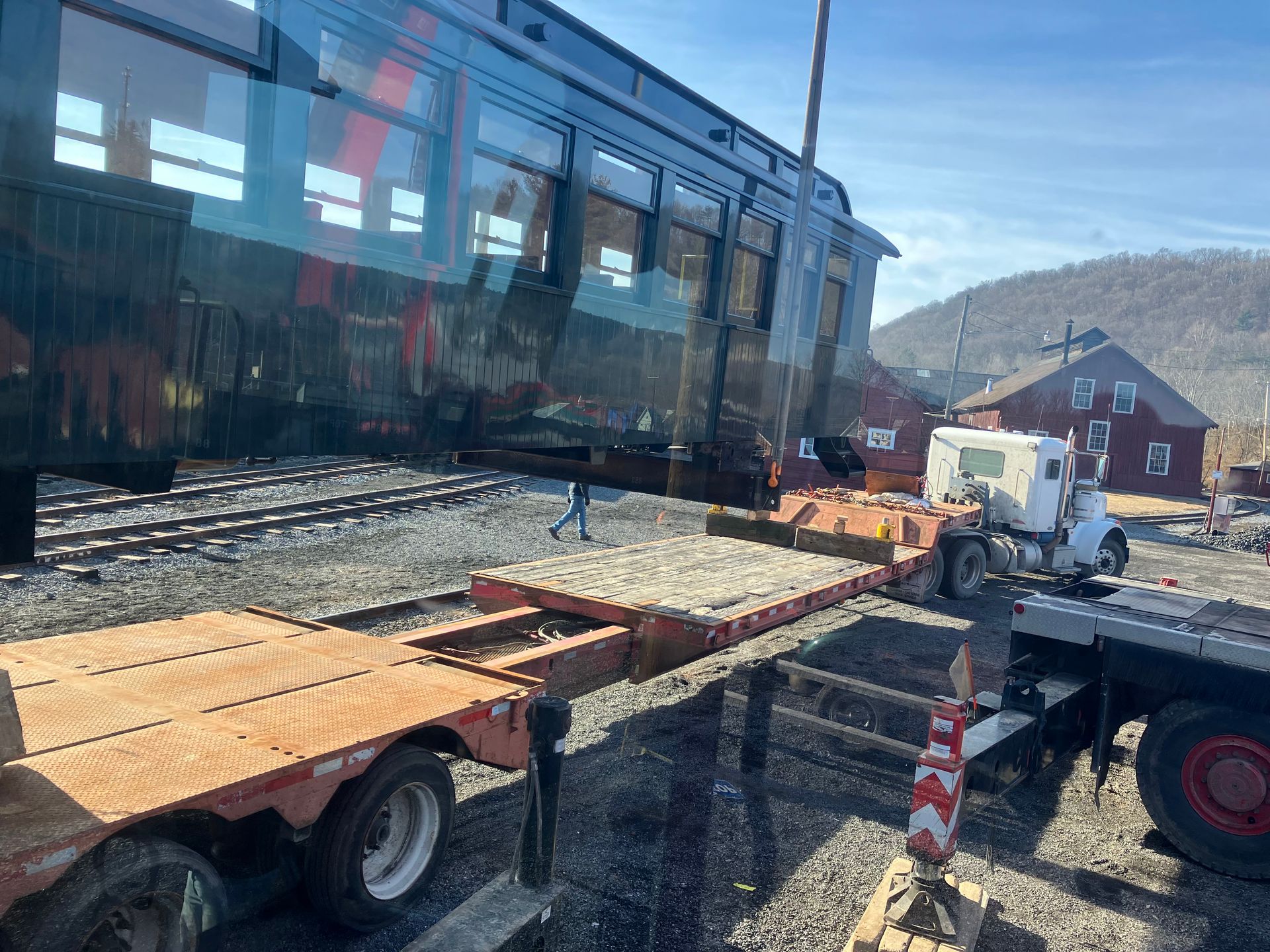 Flatbed trucks loading a black tram on railroad tracks beside a building under construction