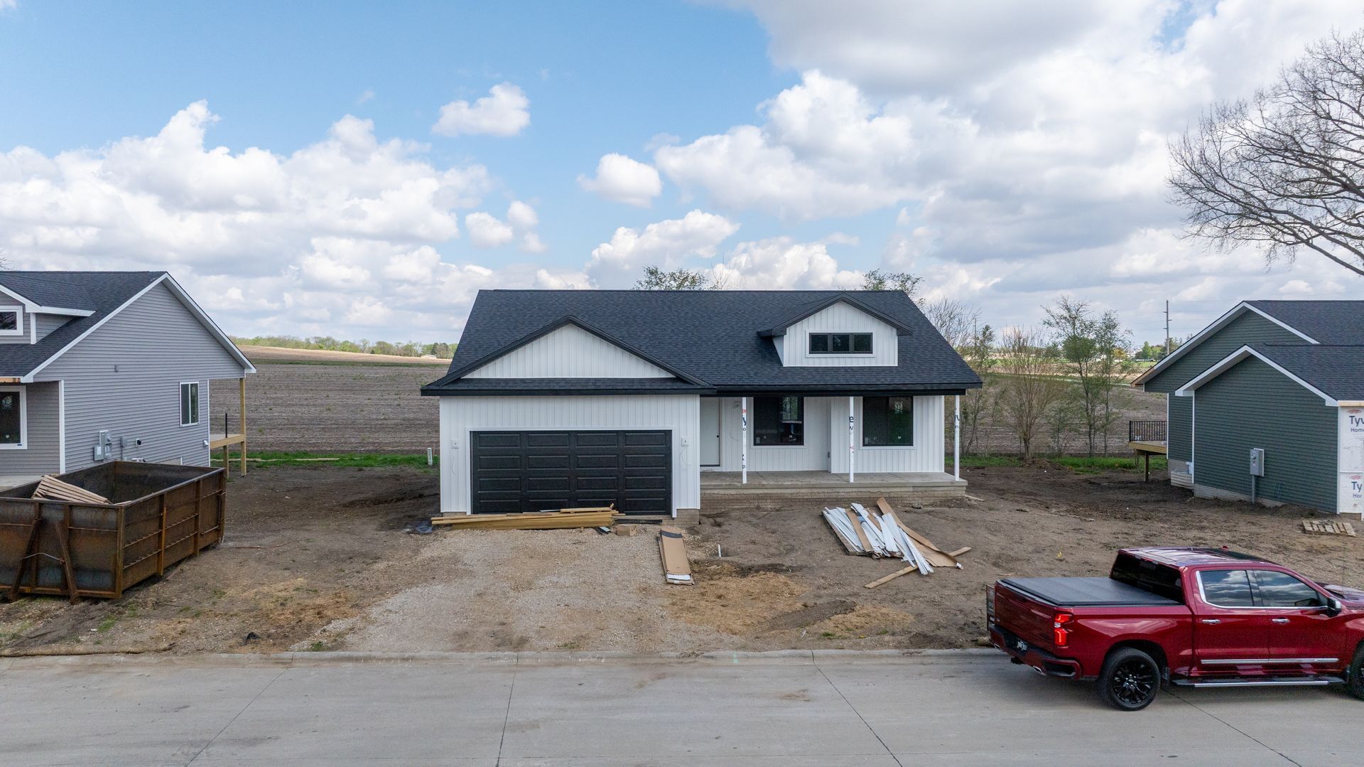 Newly built gray house with attached garage, dirt driveway, and red pickup truck in front