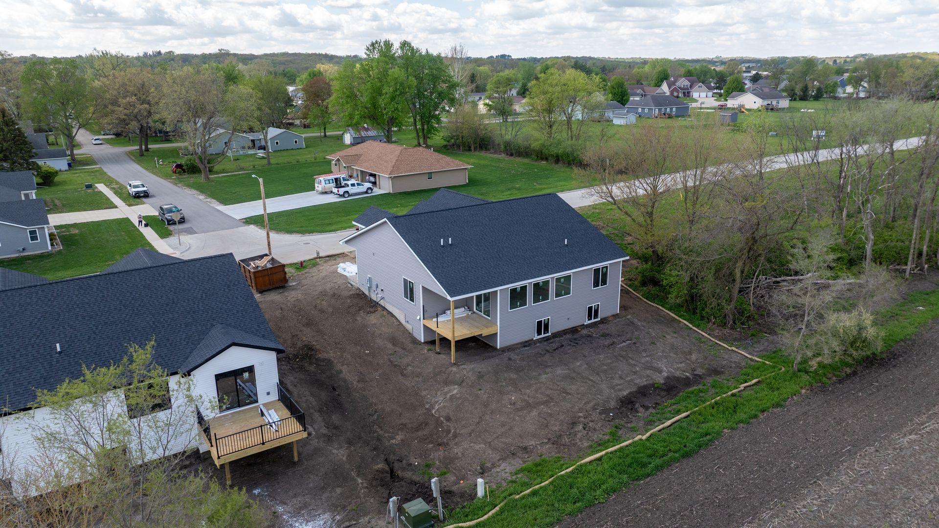 Aerial view of a new white house with dark roof beside a gravel lot and suburban homes
