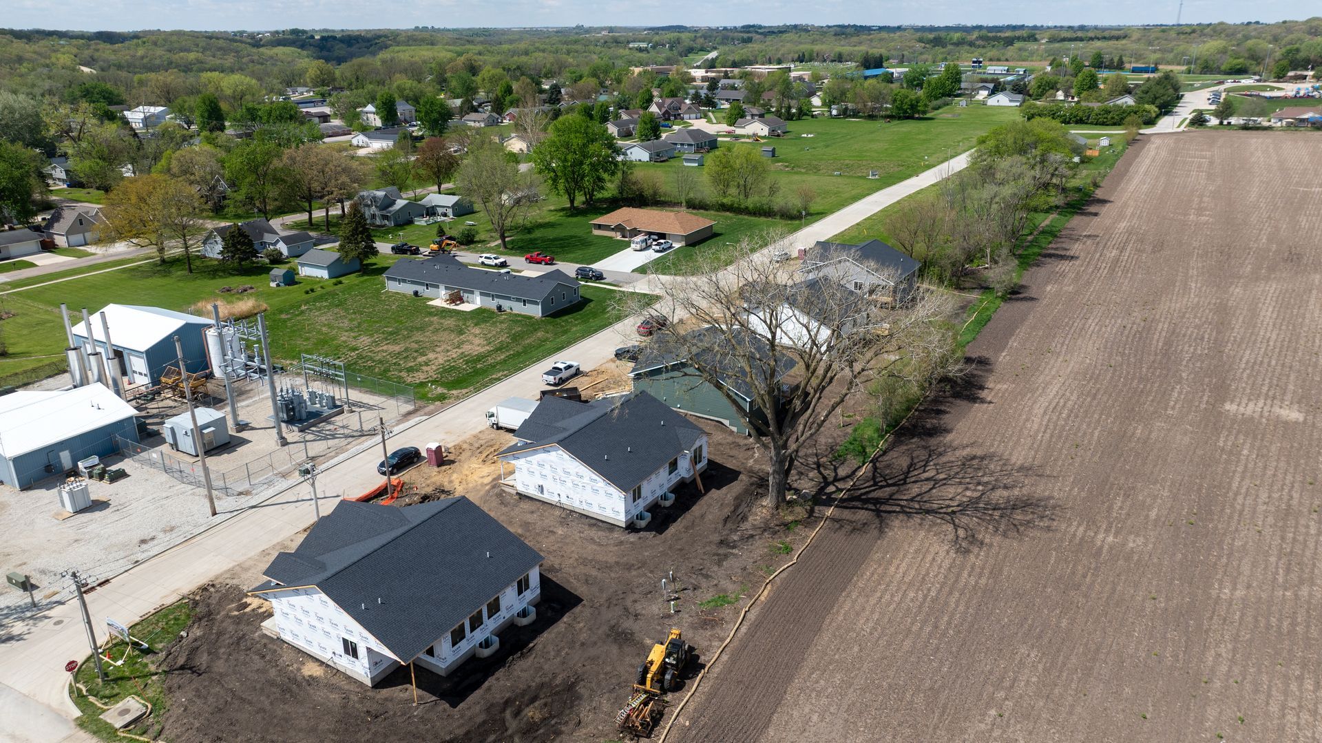Aerial view of a rural road beside farm buildings, fields, and scattered houses in a green landscape