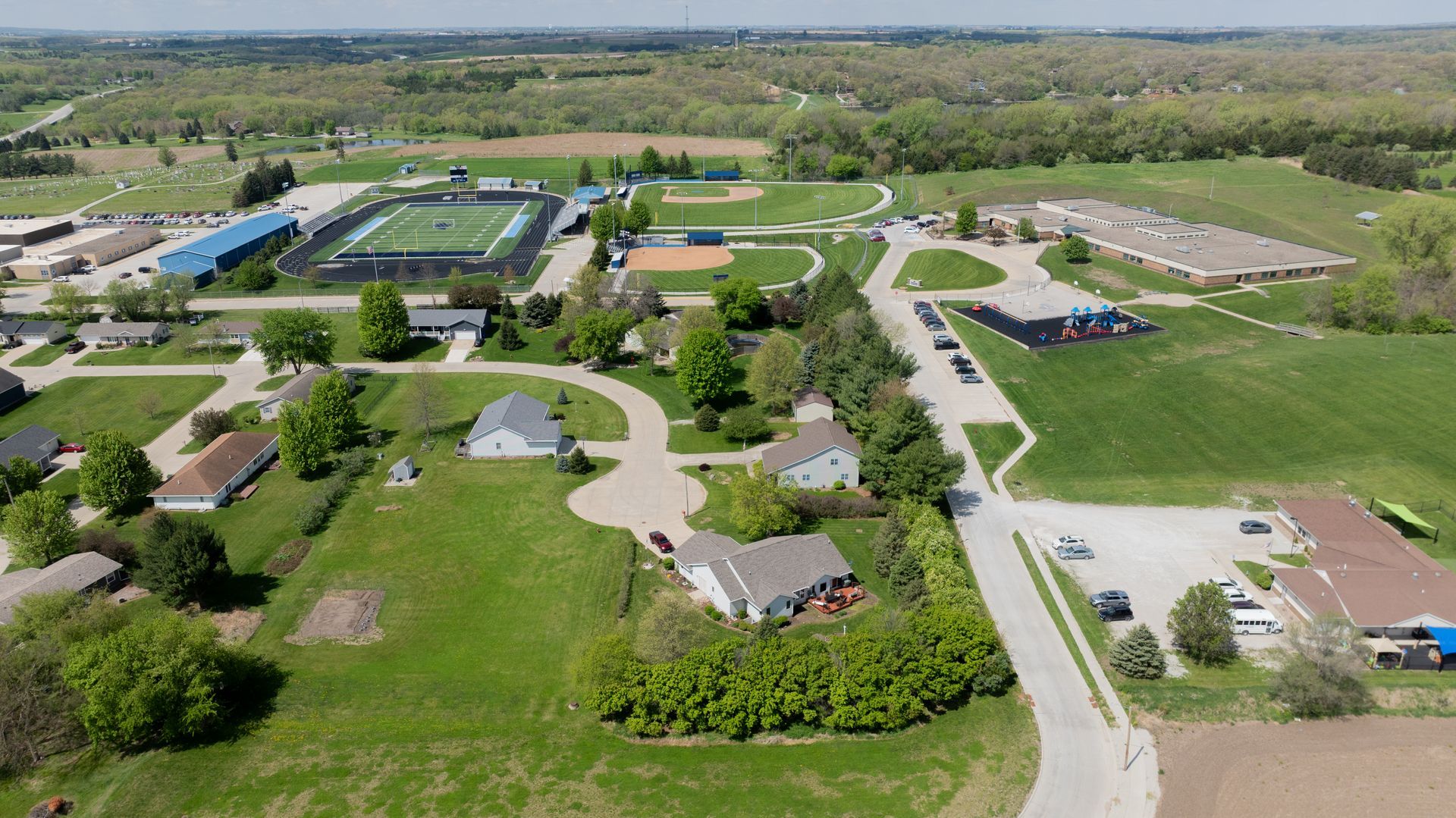 Aerial view of a rural campus with buildings, winding roads, and green fields under a clear sky