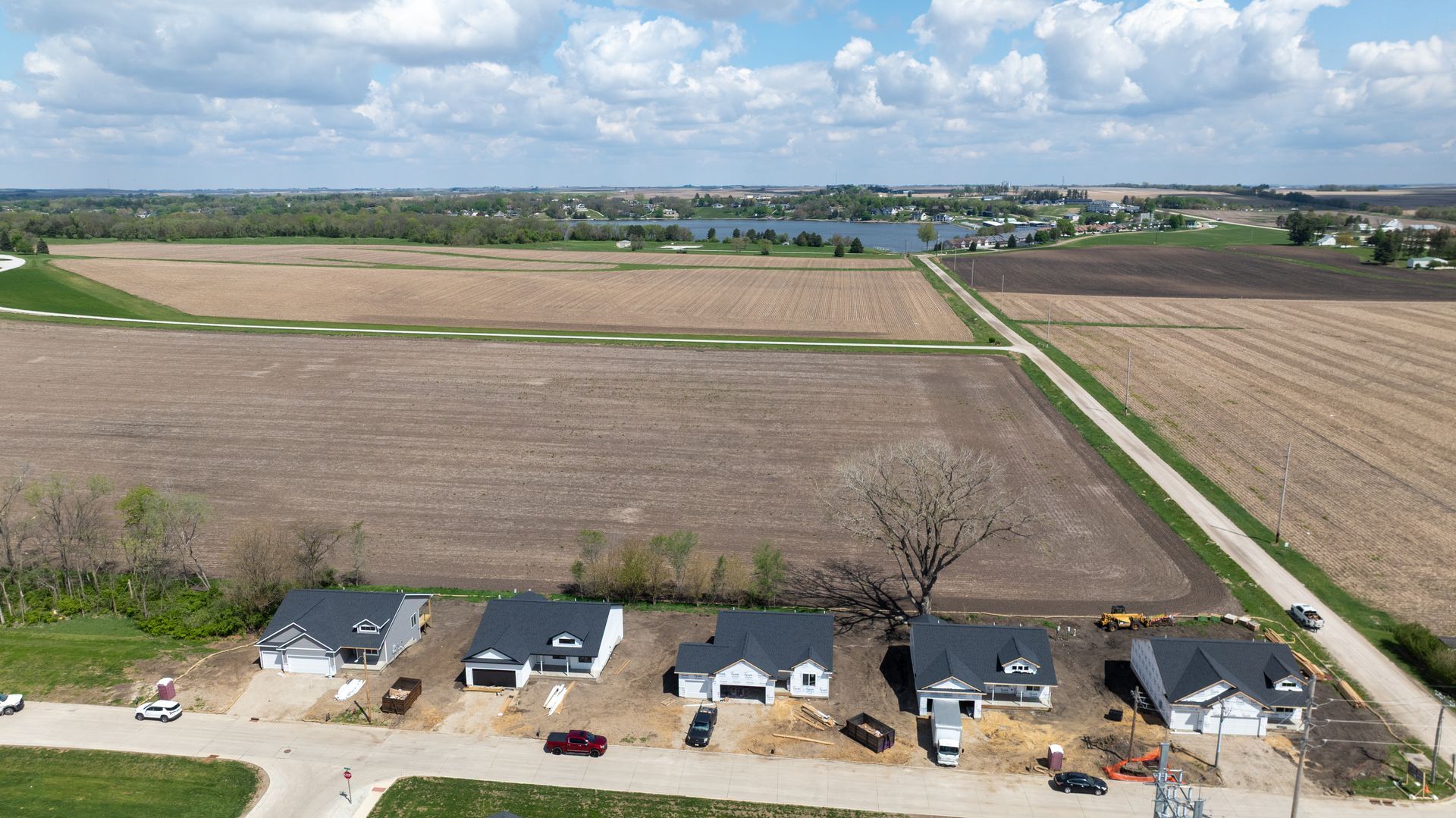 Aerial view of farmland with a row of houses along a road under a cloudy sky