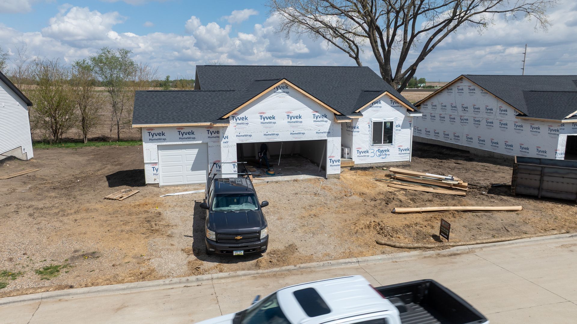 New house under construction with black SUV parked in front and a white vehicle at the bottom edge