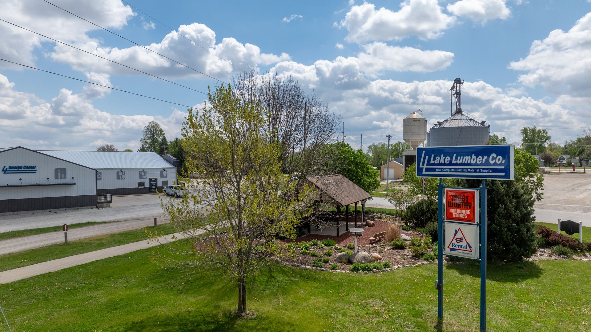 Pathway signs at a landscaped farmstead with a pond, trees, and blue sky with clouds