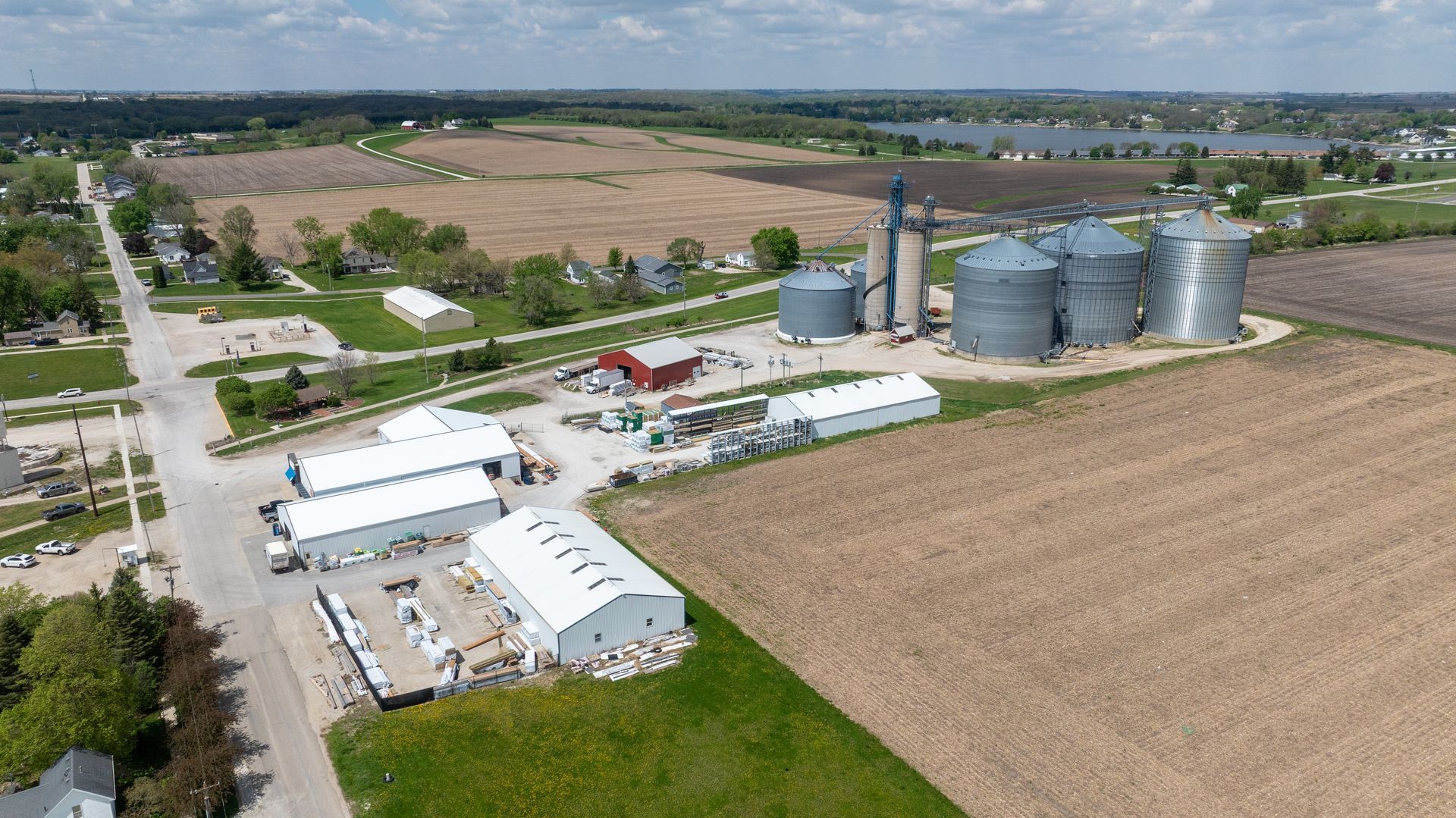 Aerial view of a farm with white buildings, grain silos, tractors, and surrounding crop fields