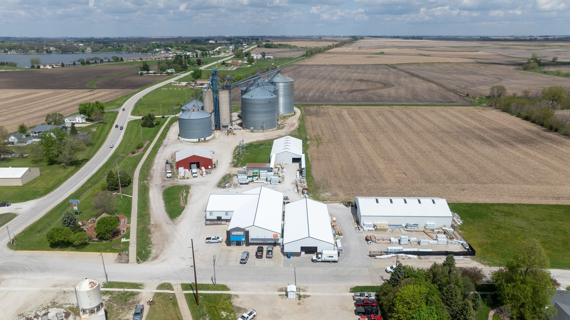 Aerial view of a rural grain processing facility with silos, white buildings, and surrounding farmland.