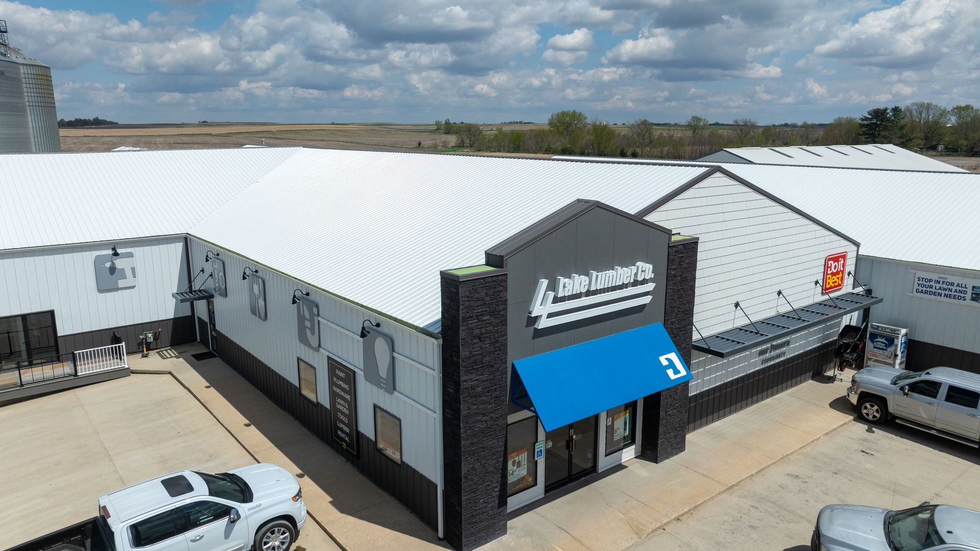 Aerial view of a white industrial building with a blue awning and parked vehicles outside.