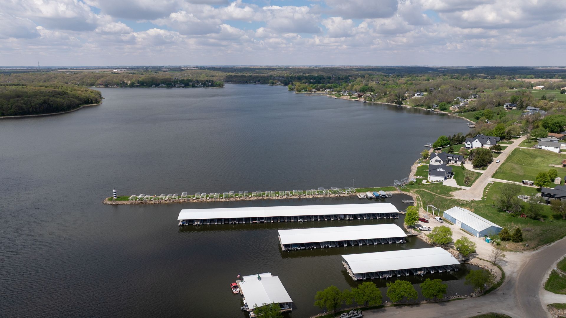 Aerial view of a calm lake with docks, shoreline homes, and a cloudy sky.