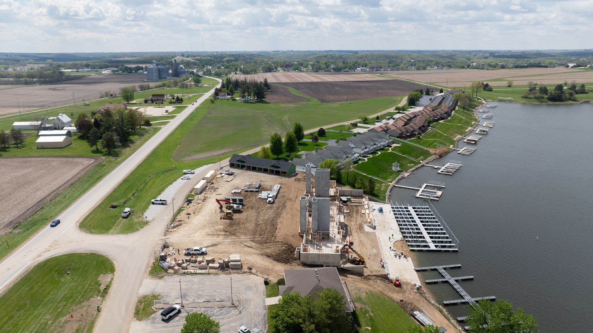 Aerial view of a riverside marina, construction site, and road beside farmland.