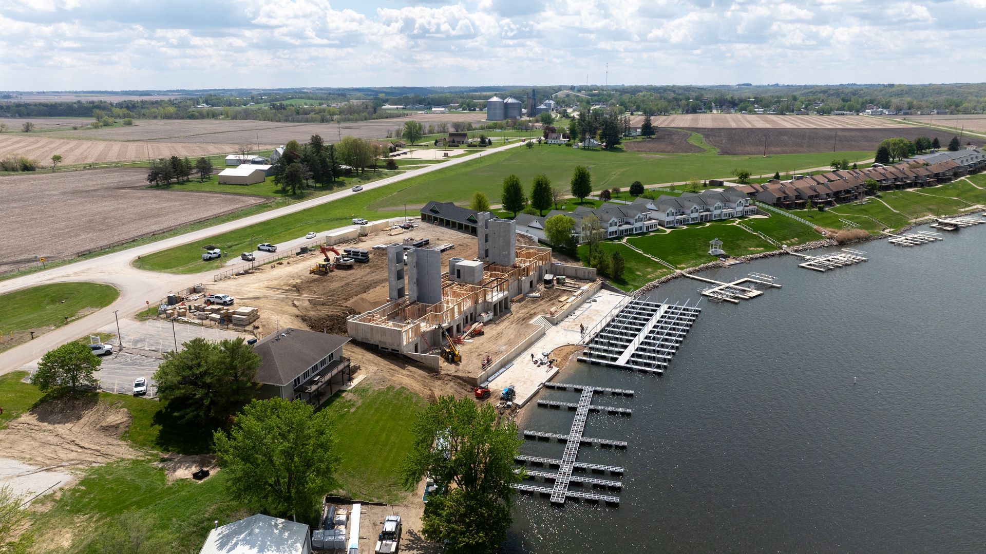 Aerial view of a marina construction site beside calm water, with docks, cranes, and parked vehicles.