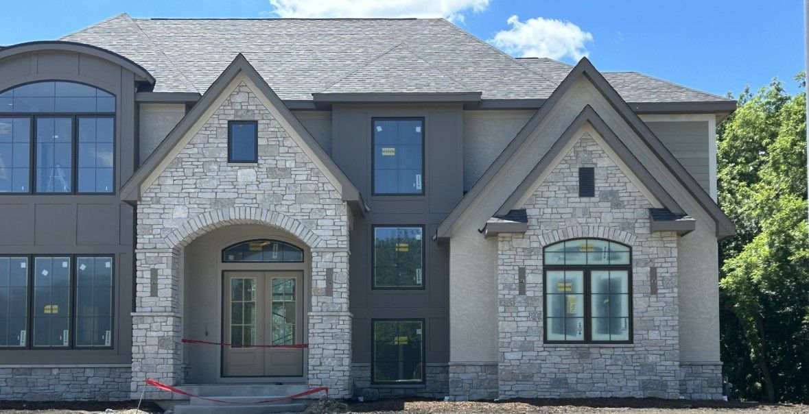 Stone-and-brick suburban house exterior with gabled roof and arched entryway under a clear blue sky