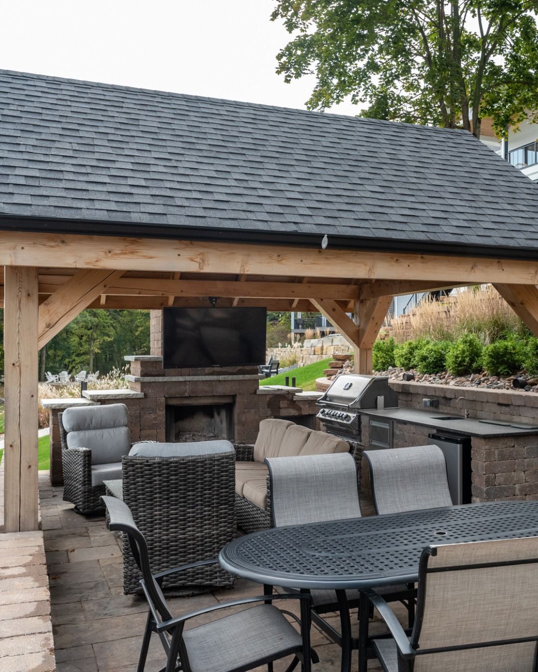 An outdoor covered patio featuring a stone fireplace with a mounted TV, wicker seating, and a dining table.
