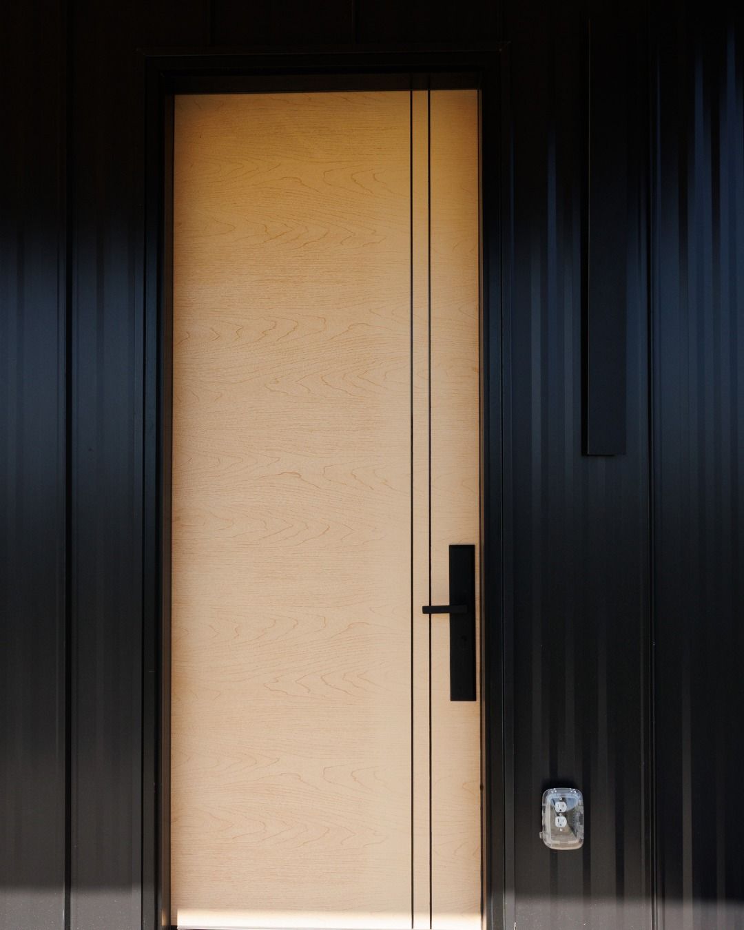 Modern black front door with a warm-lit glass panel and metal handle