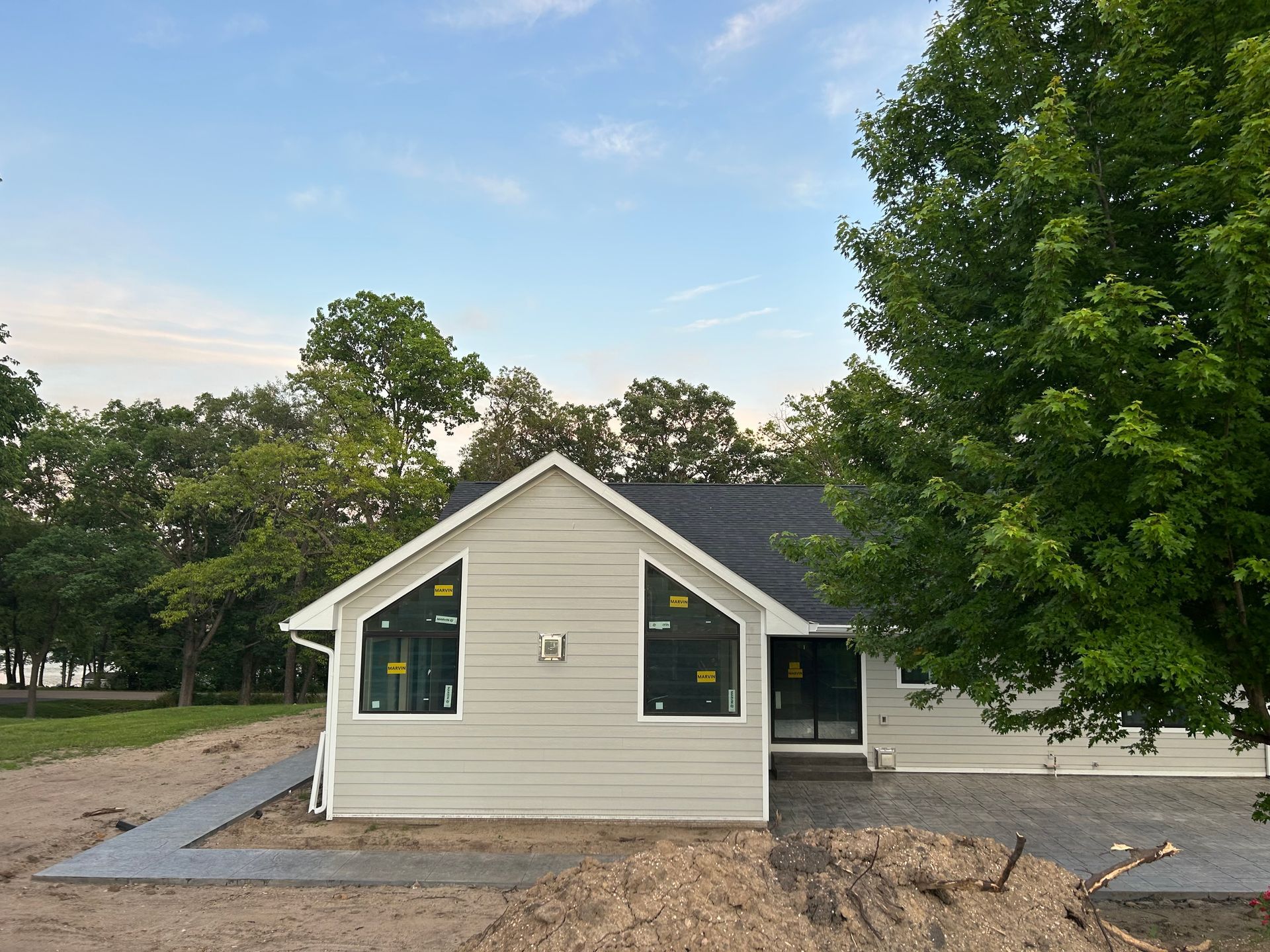 Small beige house with dark roof, new gravel path, and trees under a blue sky.