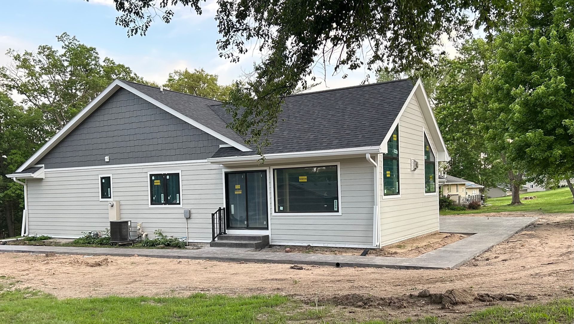 Small gray single-story house with dark roof, front porch, and a gravel driveway under trees
