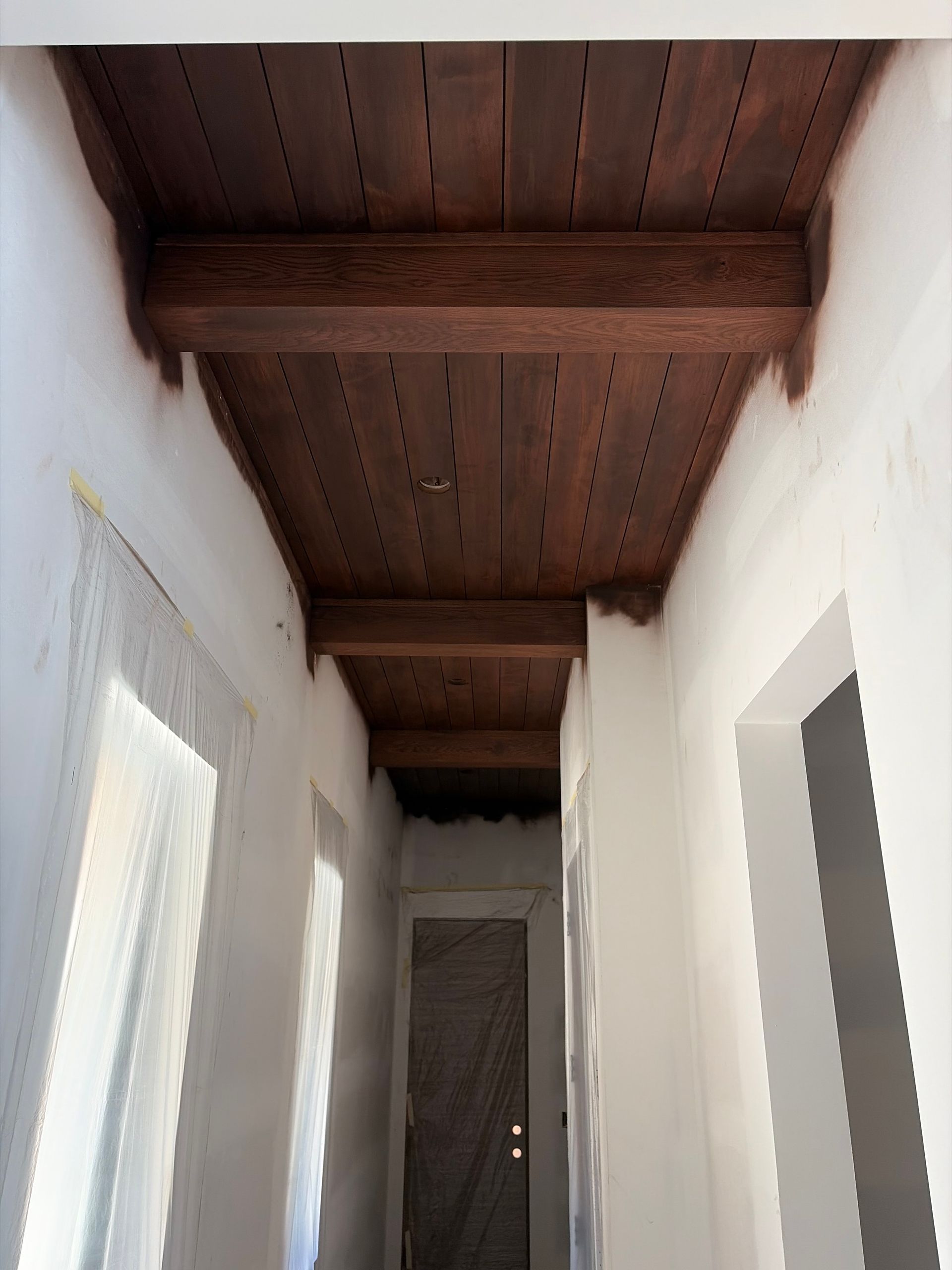 Narrow white hallway with exposed wooden ceiling beams and a door at the far end