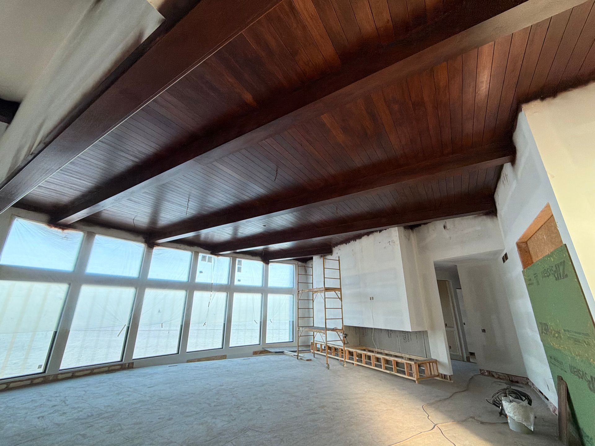 Spacious unfinished room with wood ceiling, large windows, ladder, and stacked chairs along the wall.