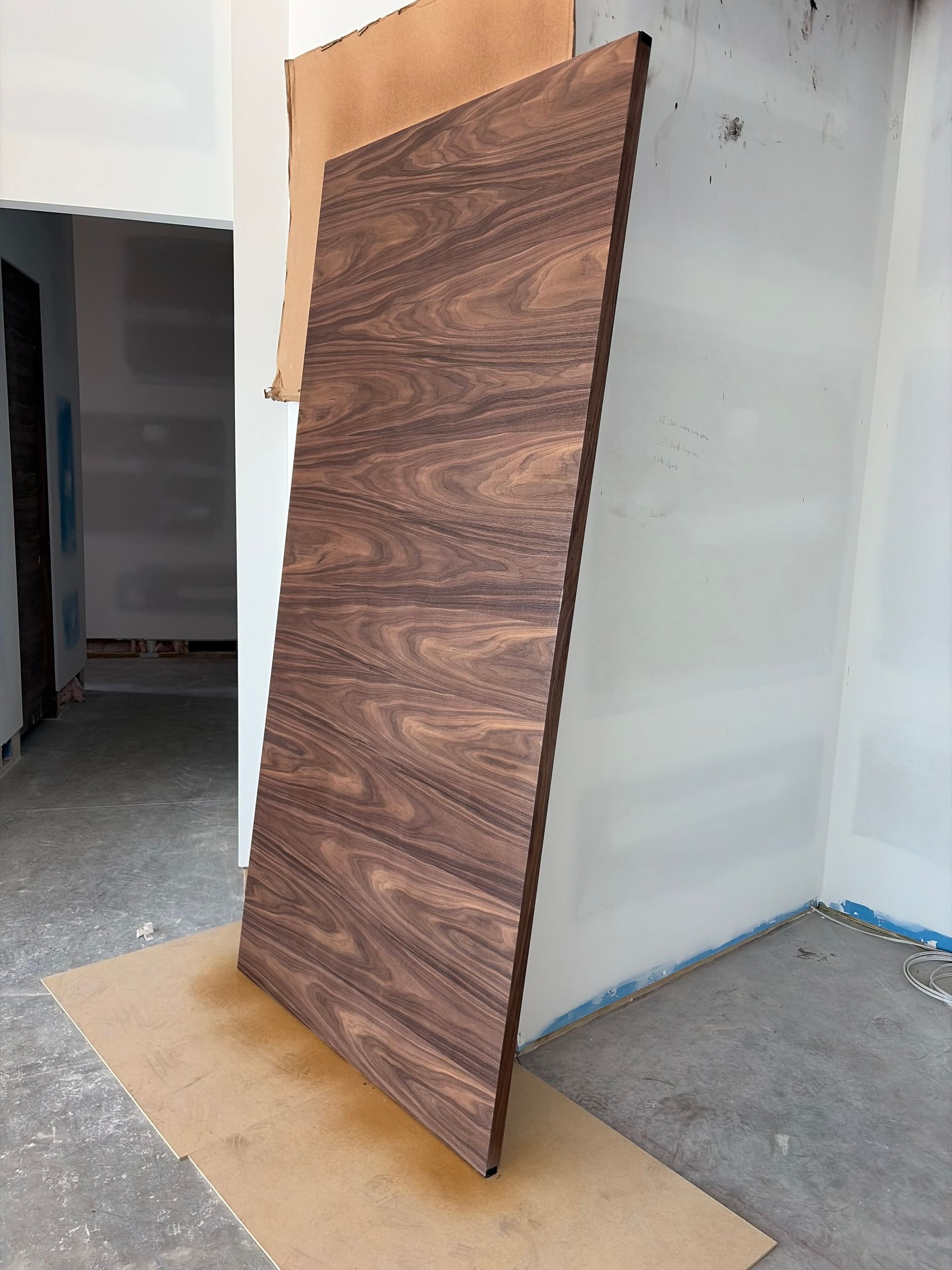 Wood-patterned door slab leaning against a wall in a bare room under renovation.