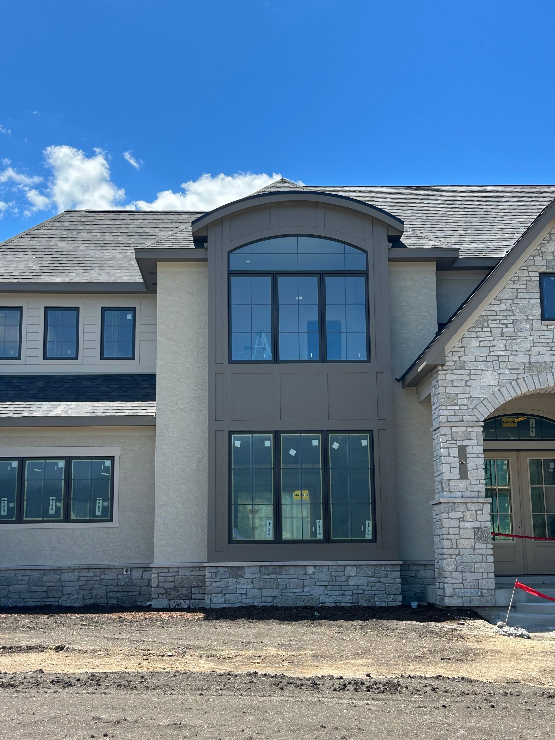 New two-story beige and stone house exterior with large front windows under a blue sky