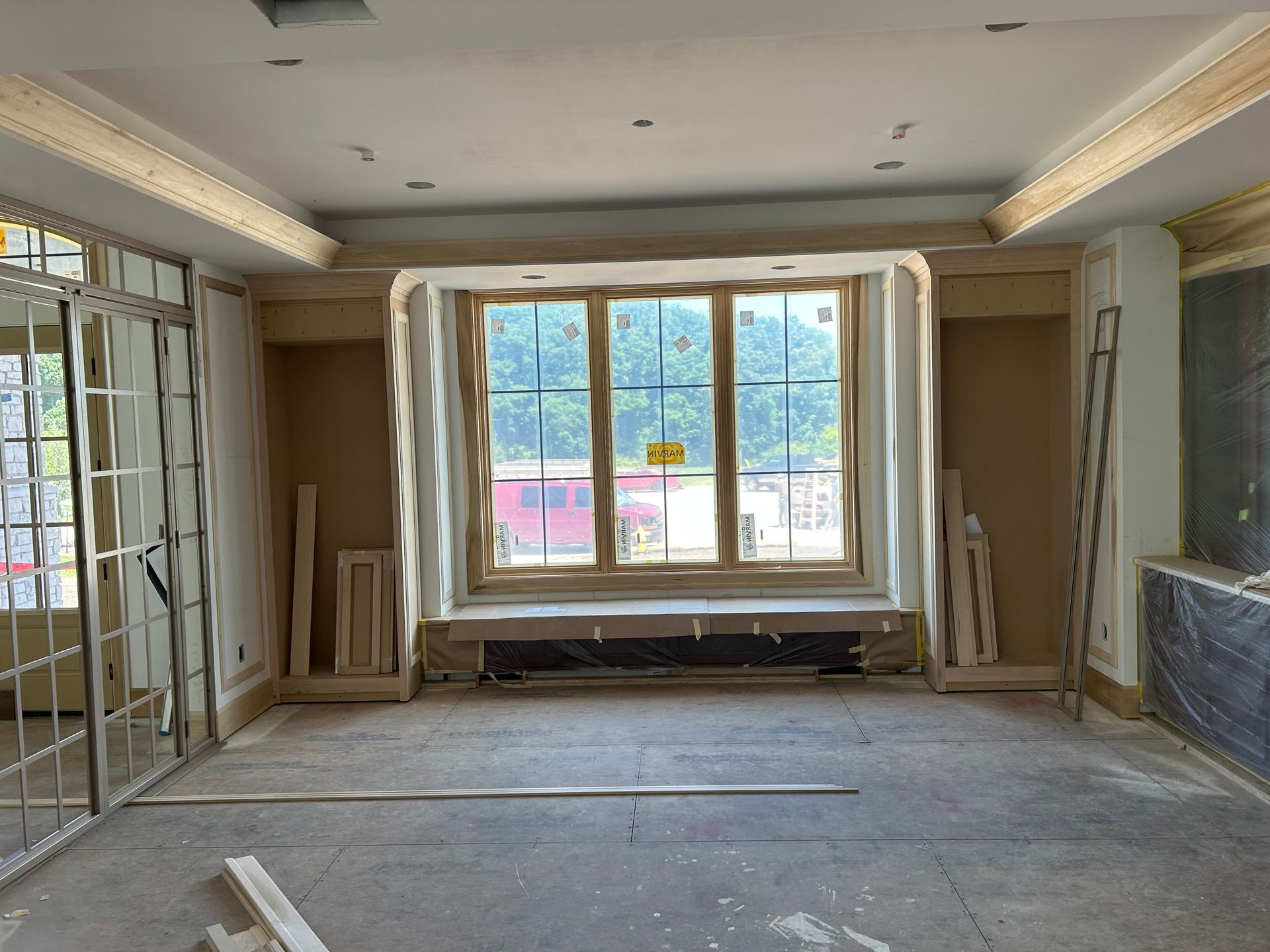 Empty living room under renovation with large bay window, exposed walls, and unfinished floor