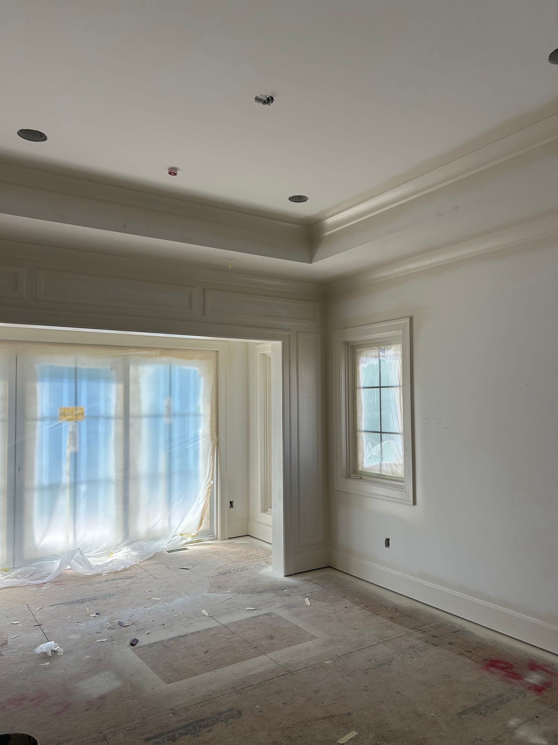 Empty unfurnished room with white walls, tray ceiling, recessed lights, and large windows with sheer curtains.