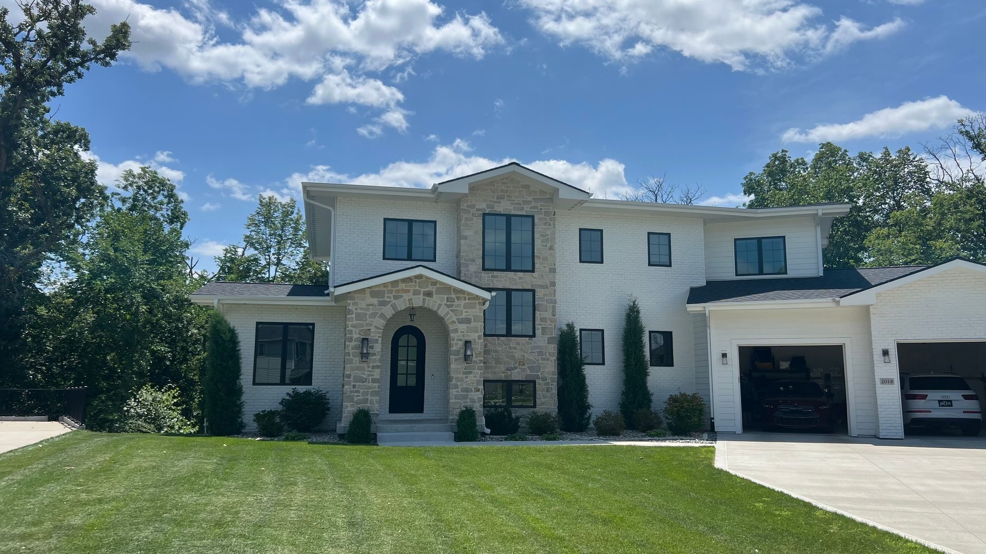 Two-story white house with stone accents, black windows, and attached garage under a blue sky.